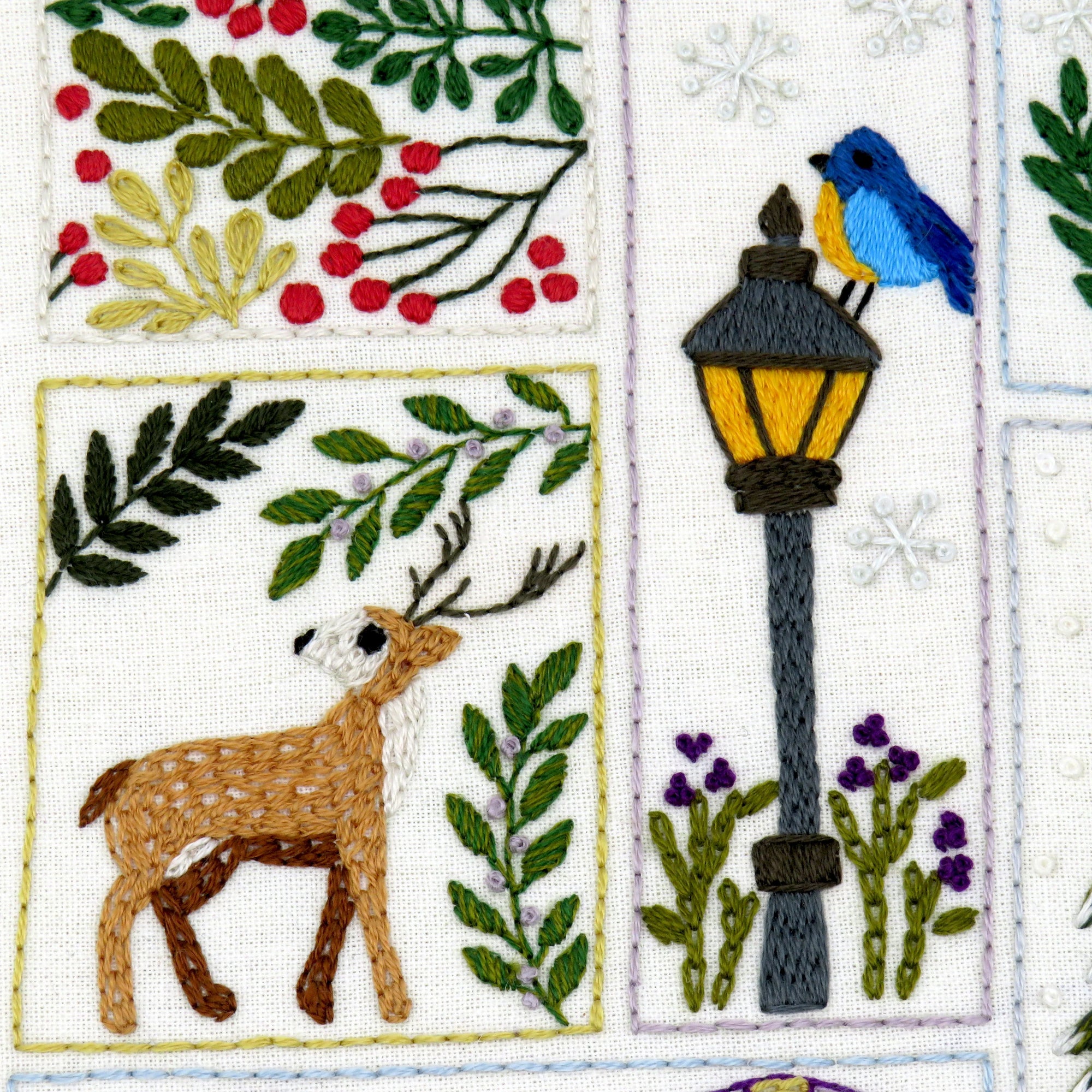 Embroidered design with deer, bird, lamp post, and foliage on a white background