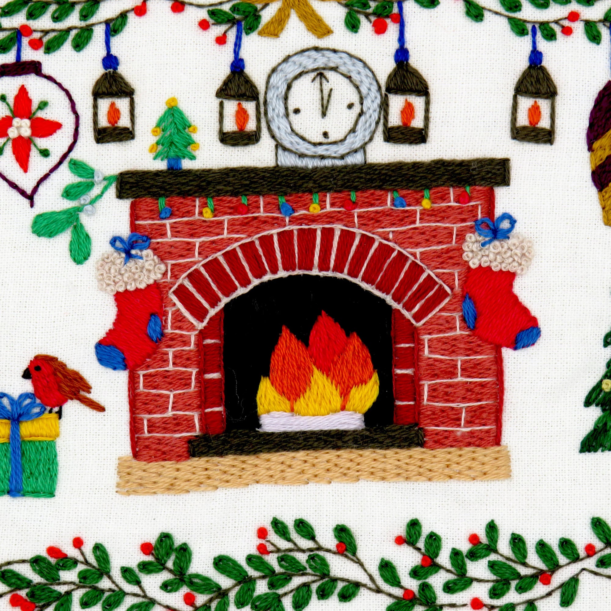 Embroidered design of a fireplace with festive elements like stockings and a clock.