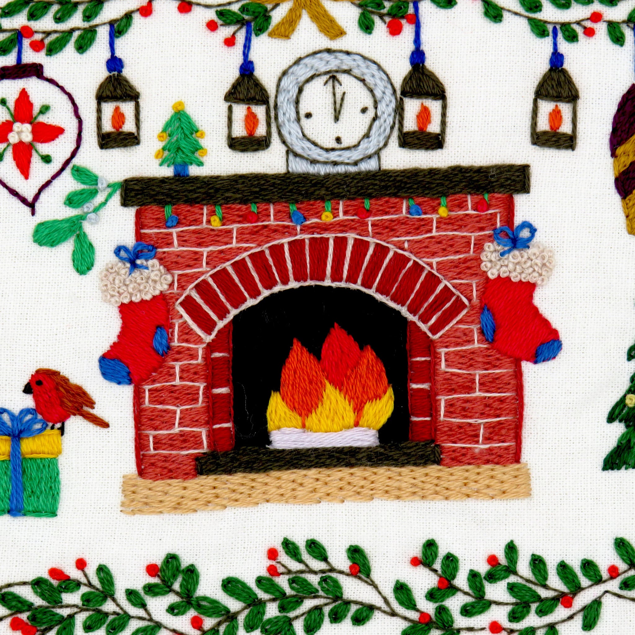 Embroidered design of a fireplace with festive elements like stockings and a clock.