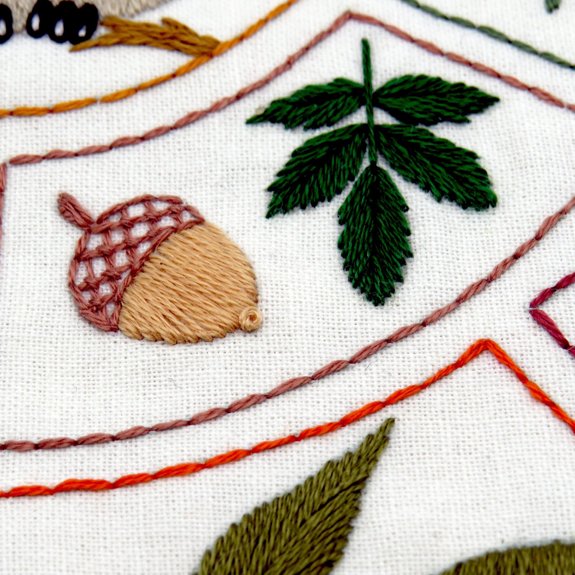 Embroidered acorn and leaves on a white fabric background