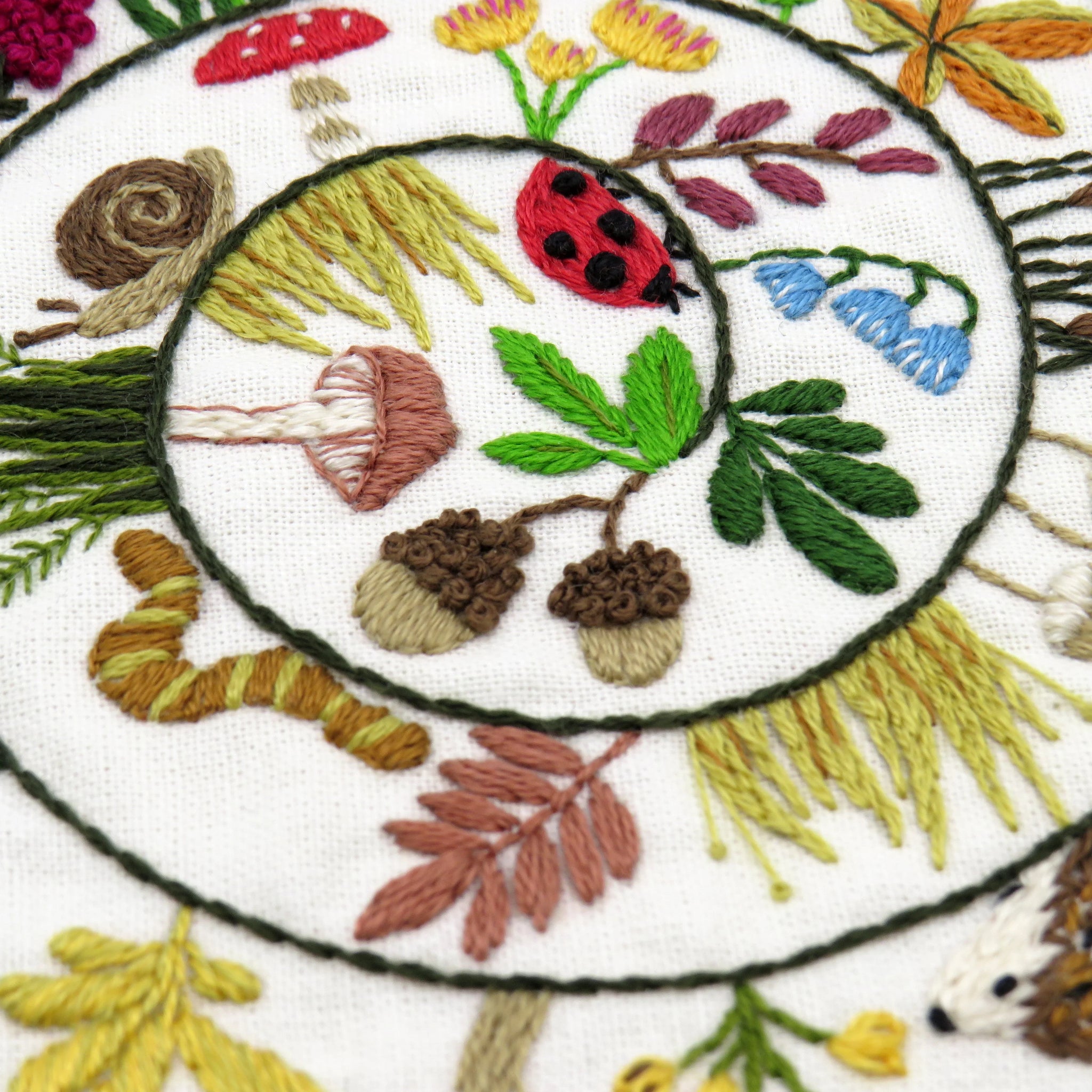Embroidered design with ladybug, acorns, and leaves on a white background