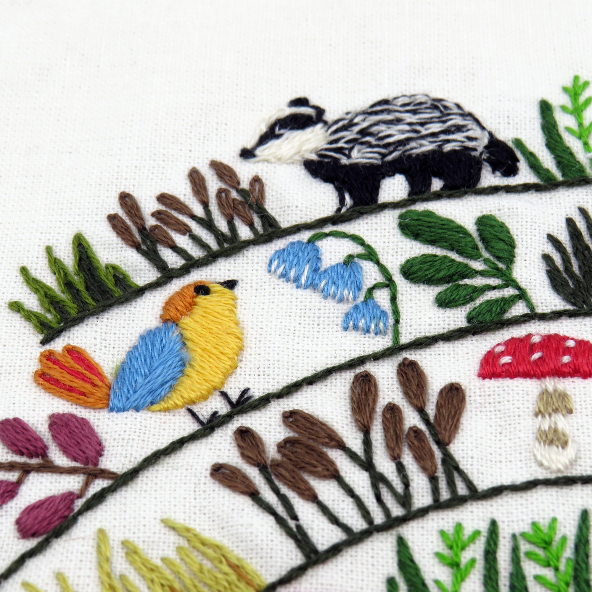 Embroidered design of a bird, badger, and plants on white fabric.