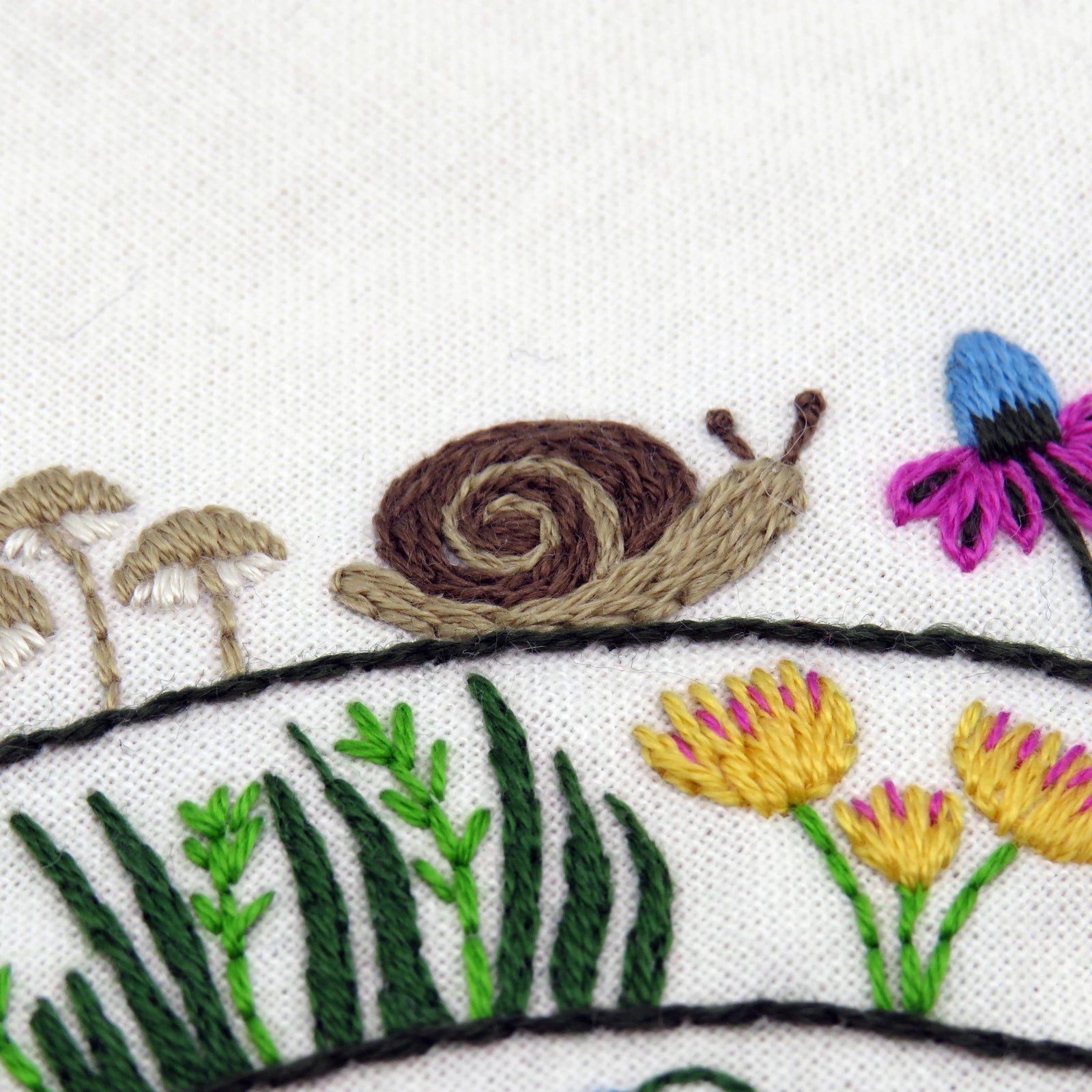 Embroidered design of a snail, flowers, and plants on white fabric.