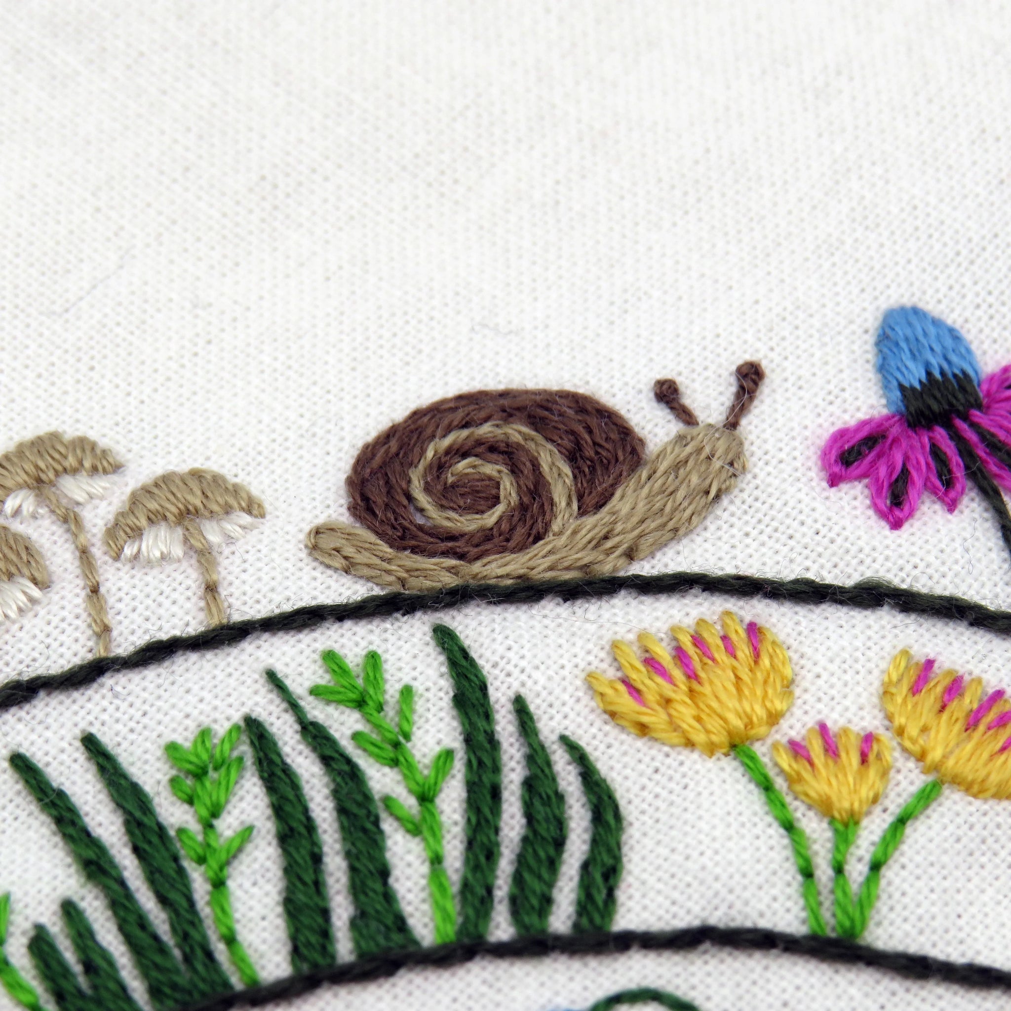 Embroidered design of a snail, flowers, and plants on white fabric.