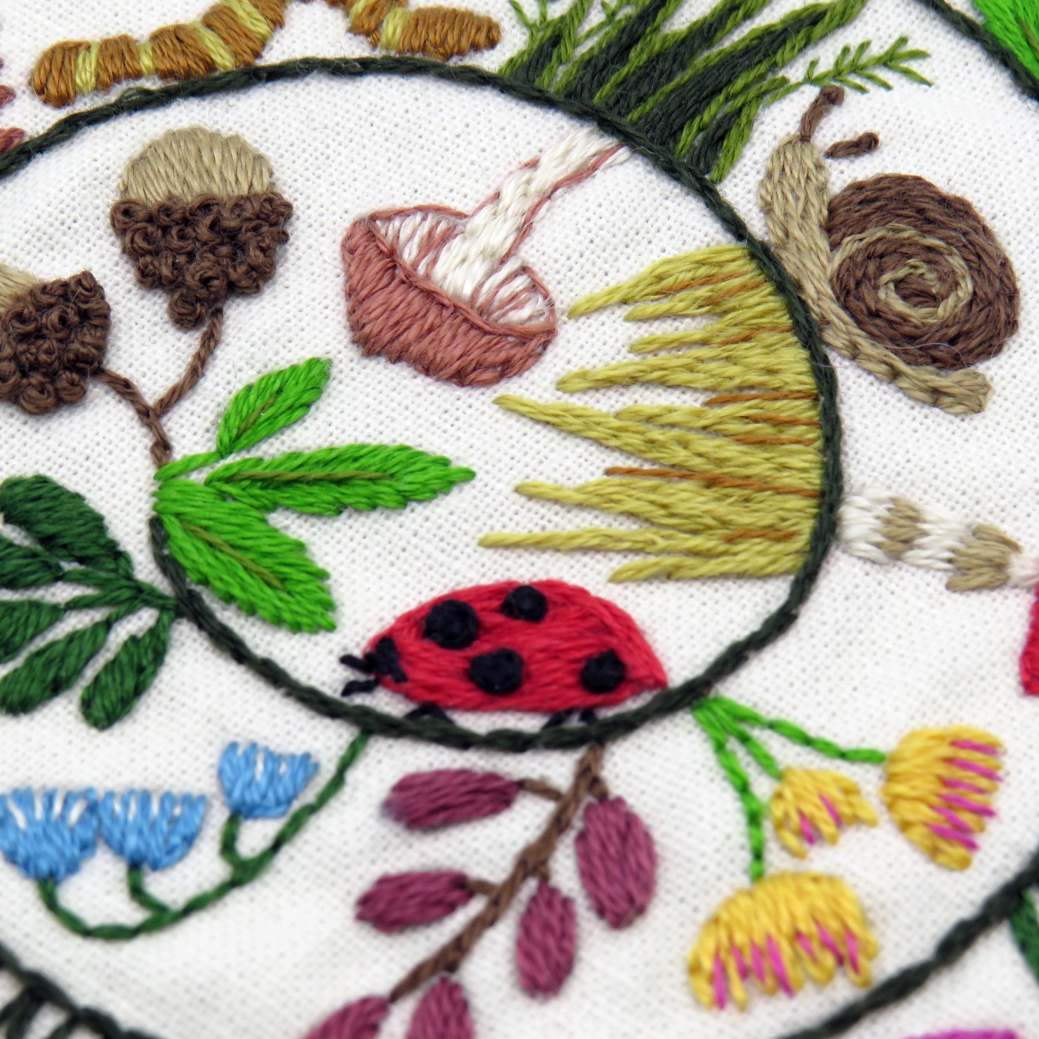 Embroidered design with a ladybug, flowers, and leaves on white fabric.
