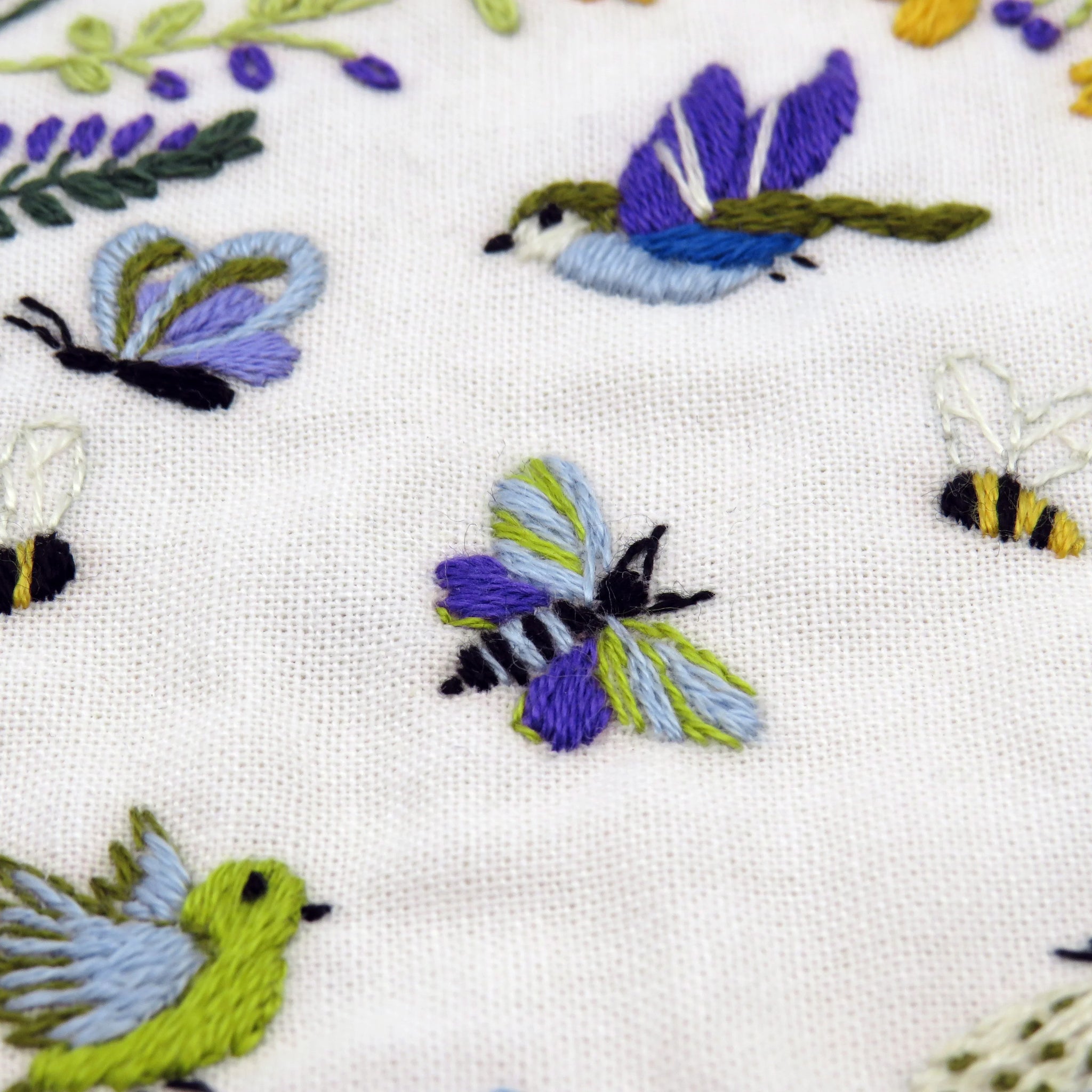 Embroidered pattern of butterflies and bees on a white fabric background