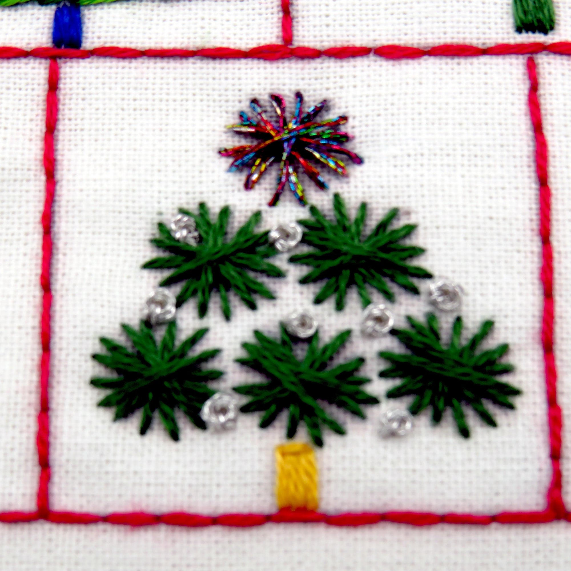 Embroidered design of a Christmas tree with green leaves, a yellow trunk, and colorful fireworks on a white background.