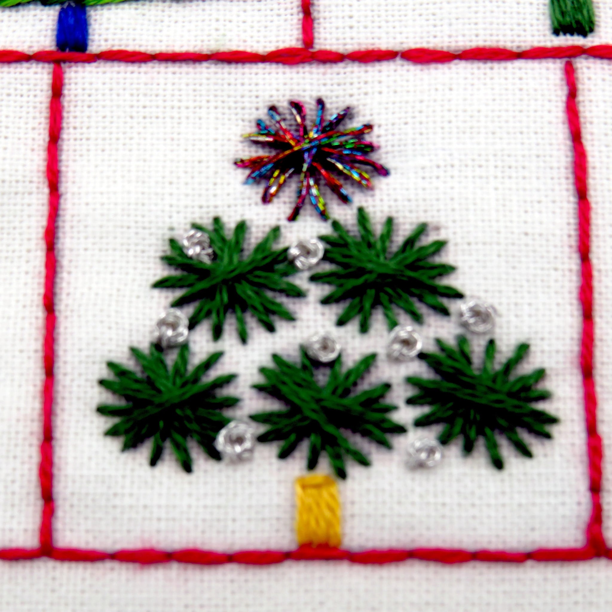Embroidered design of a Christmas tree with green leaves, a yellow trunk, and colorful fireworks on a white background.
