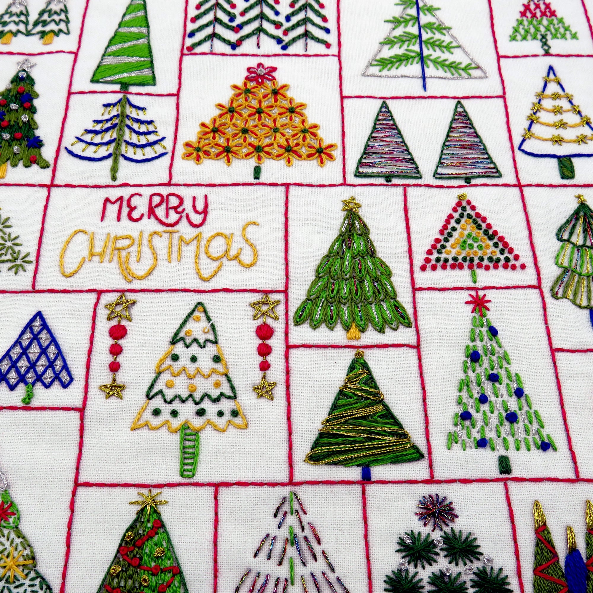 Embroidered Christmas trees and 'Merry Christmas' text on a white fabric background.