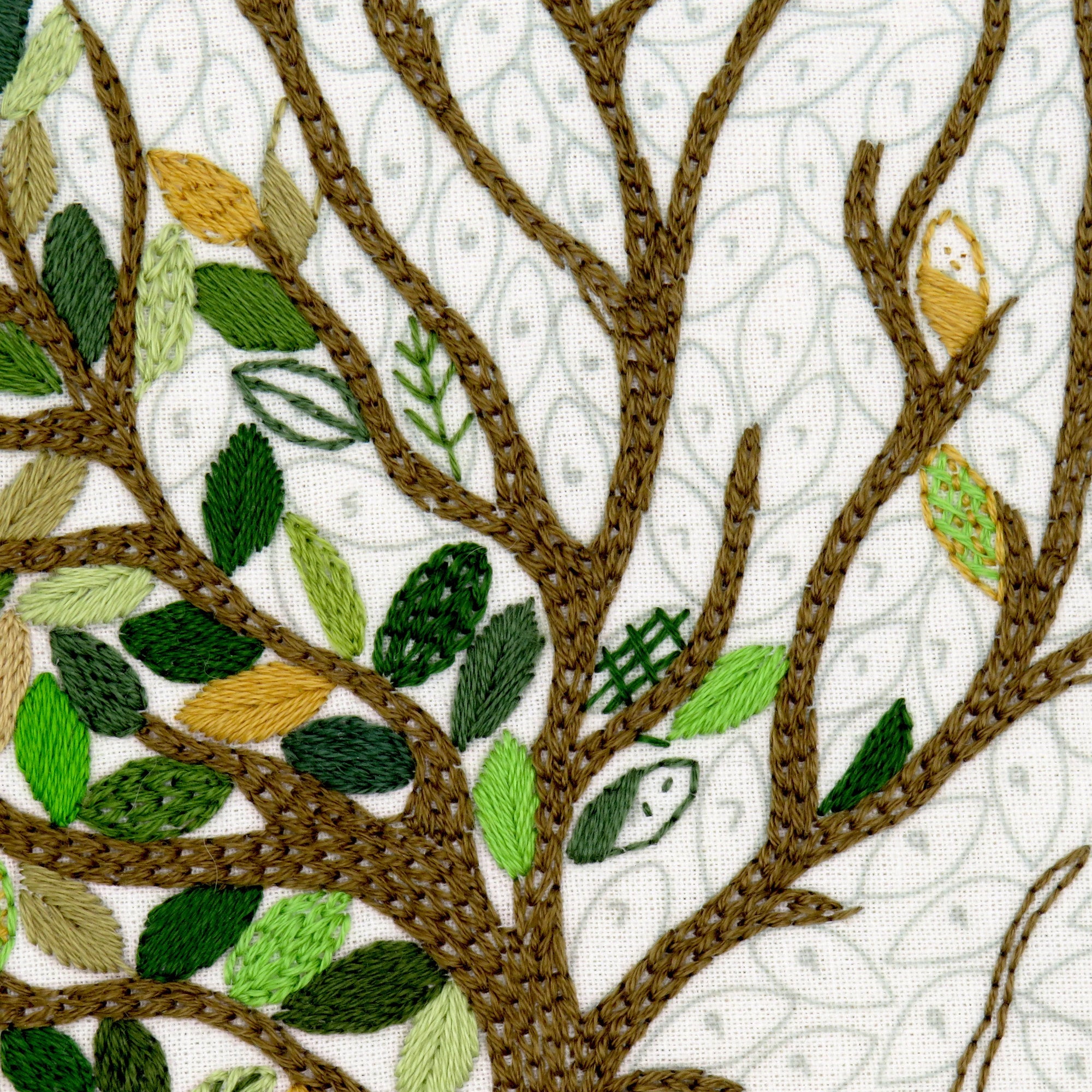 Embroidered tree design with leaves and a bird on a white background