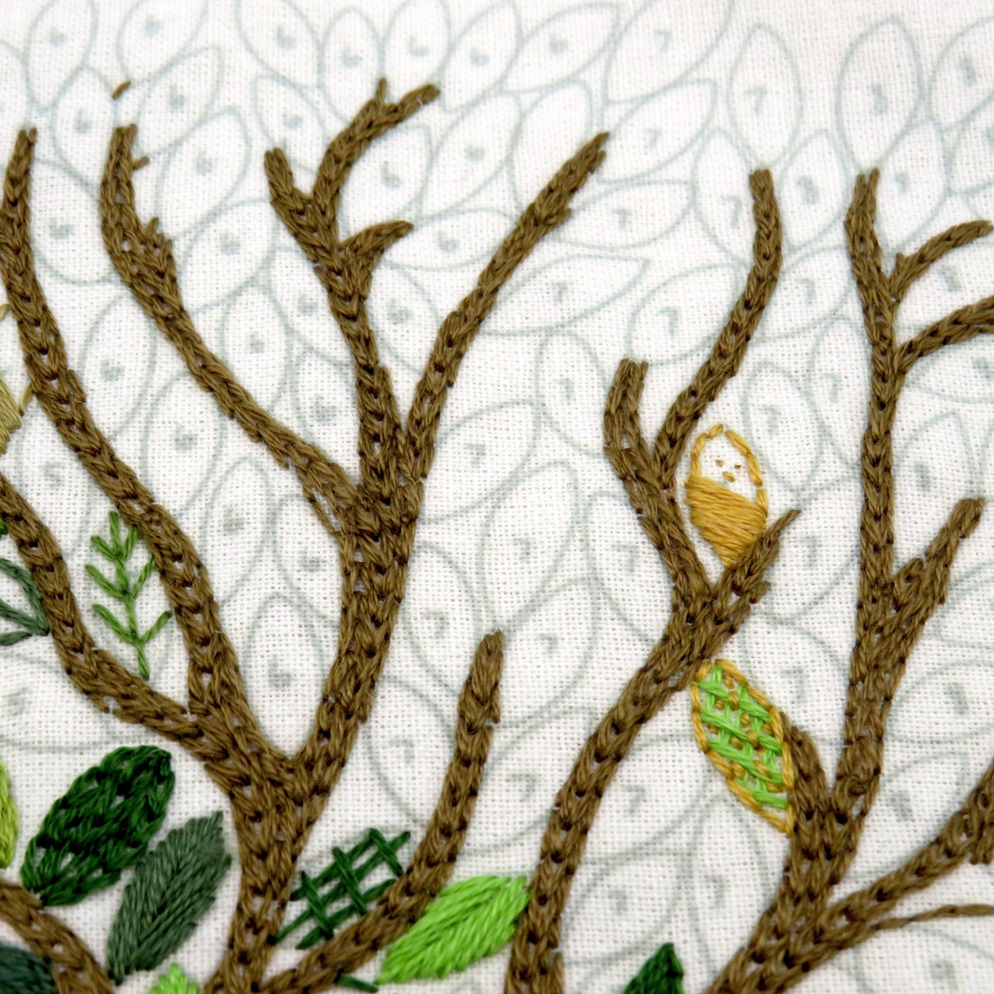 Embroidered design of tree branches with leaves and an owl on a white background