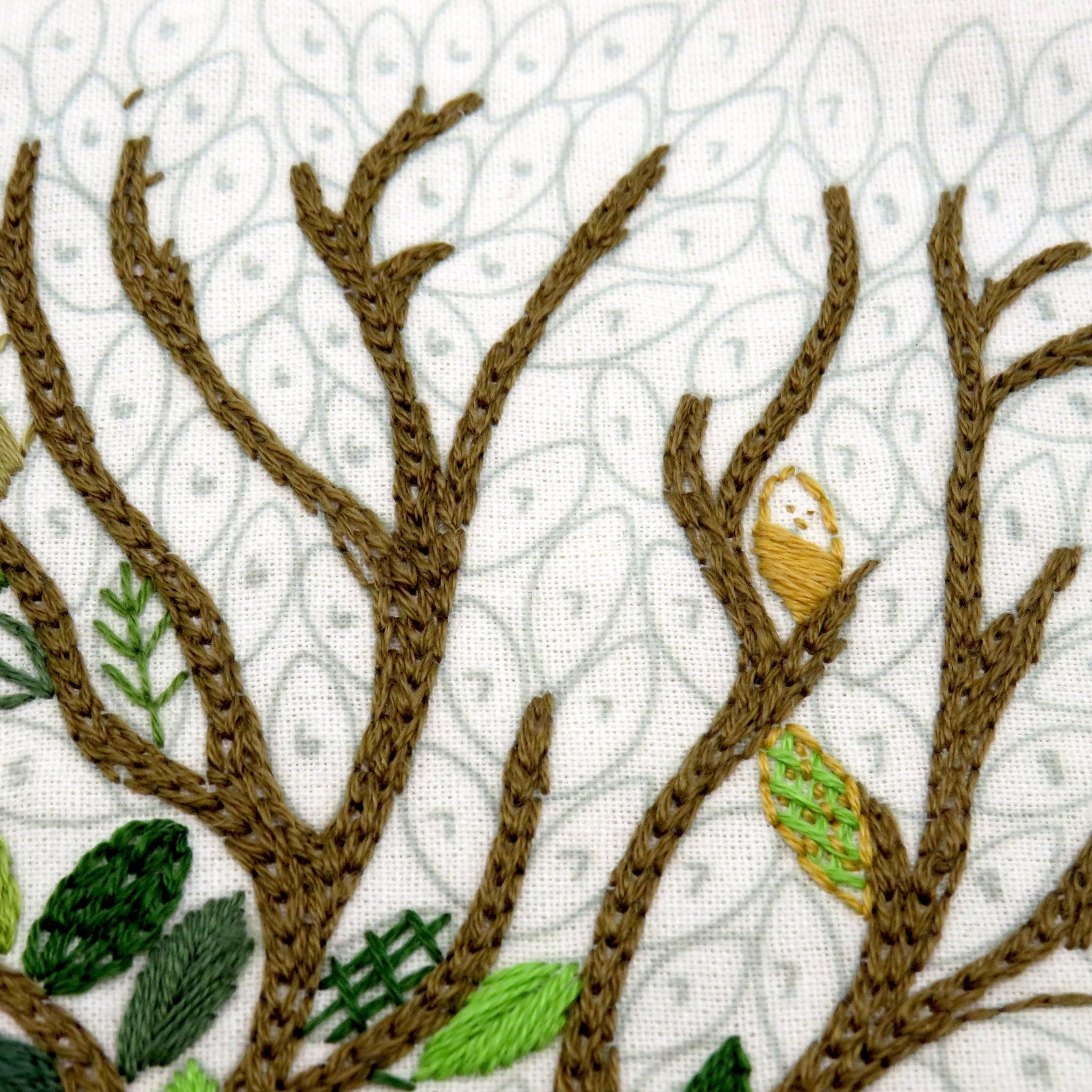 Embroidered design of tree branches with leaves and an owl on a white background