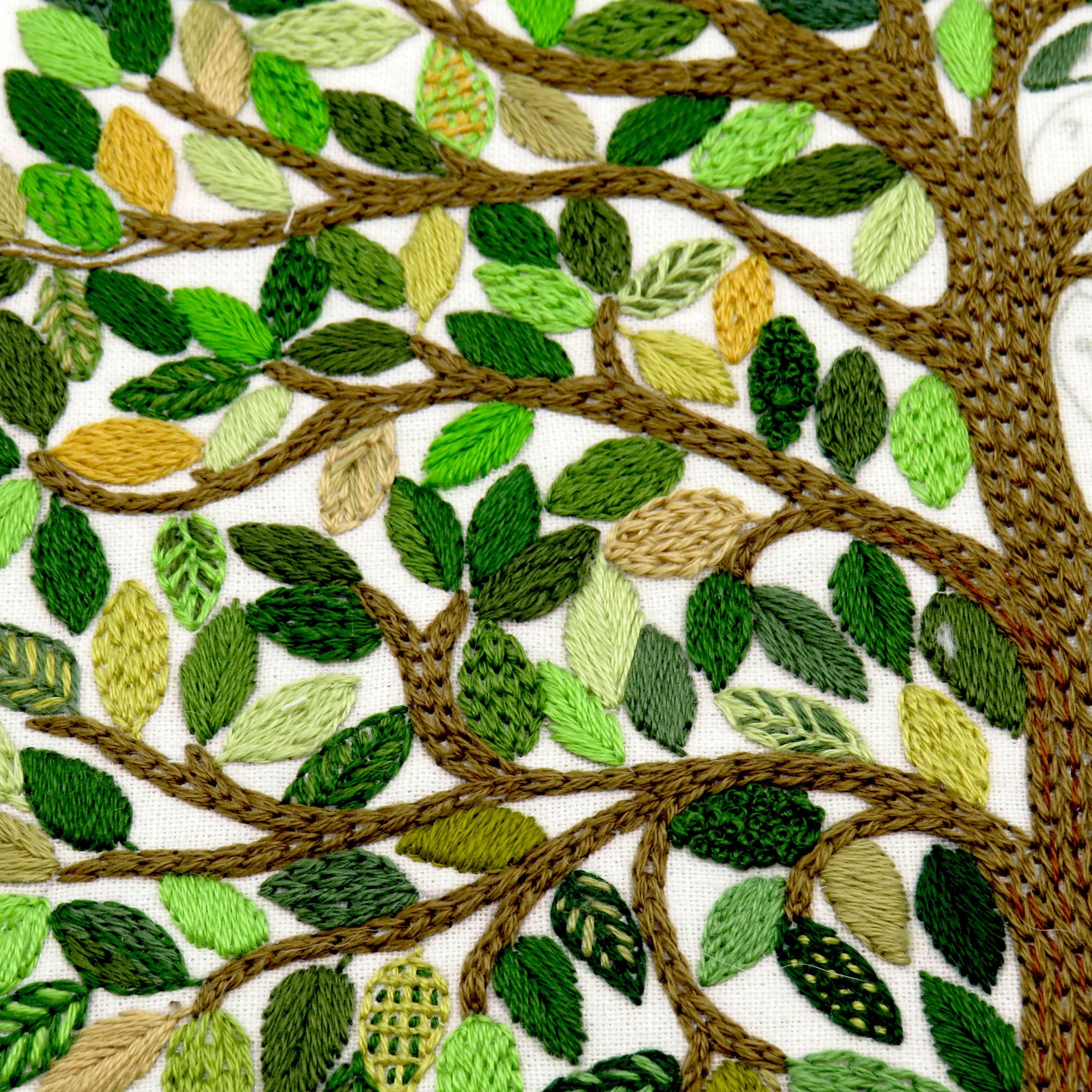 Embroidered design of a tree with green leaves and brown branches on a white background
