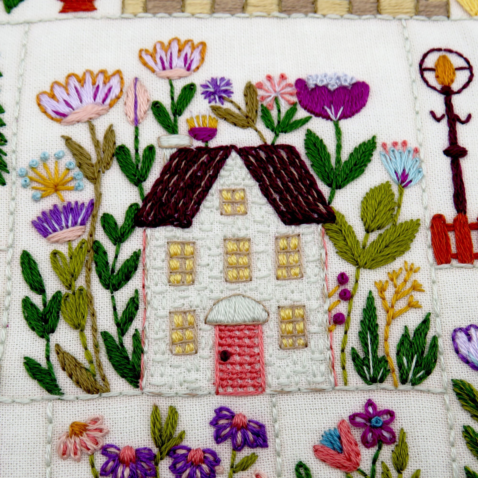Embroidered design of a house surrounded by flowers on fabric.