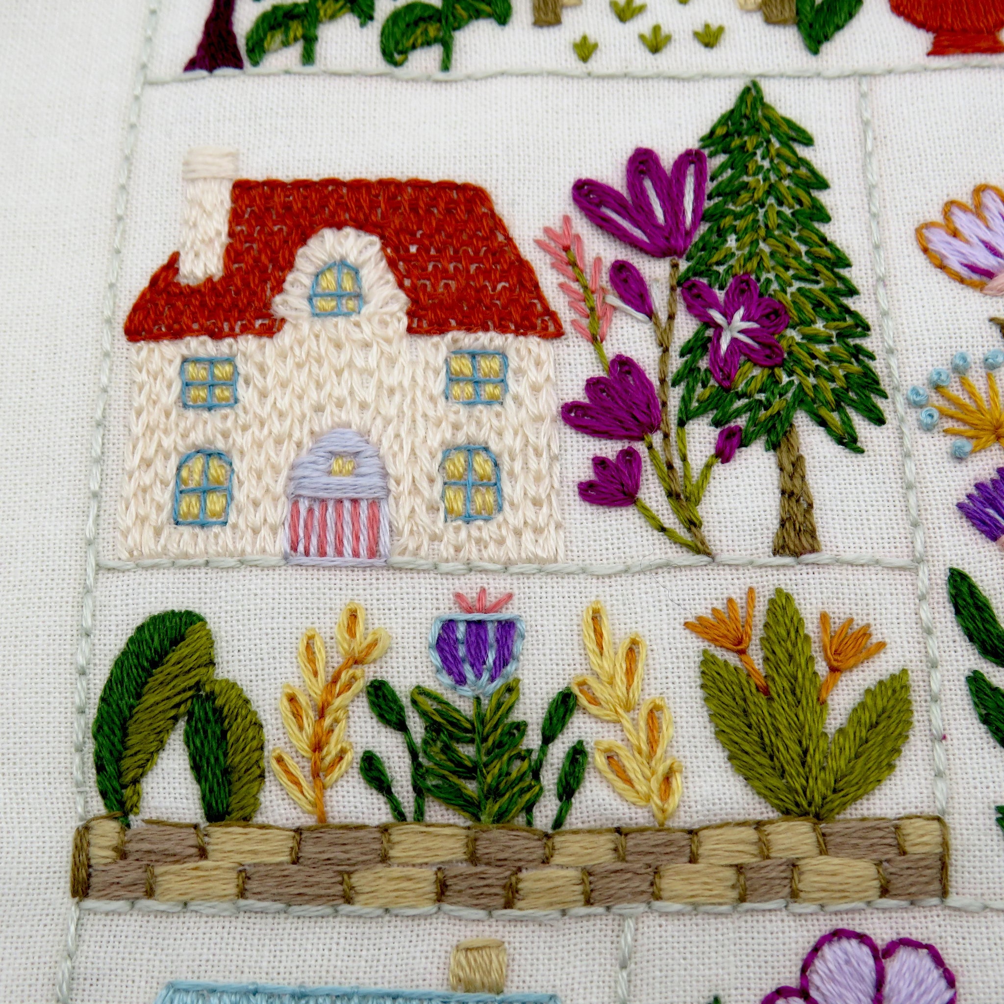 Embroidered scene with a house, trees, and flowers on fabric.