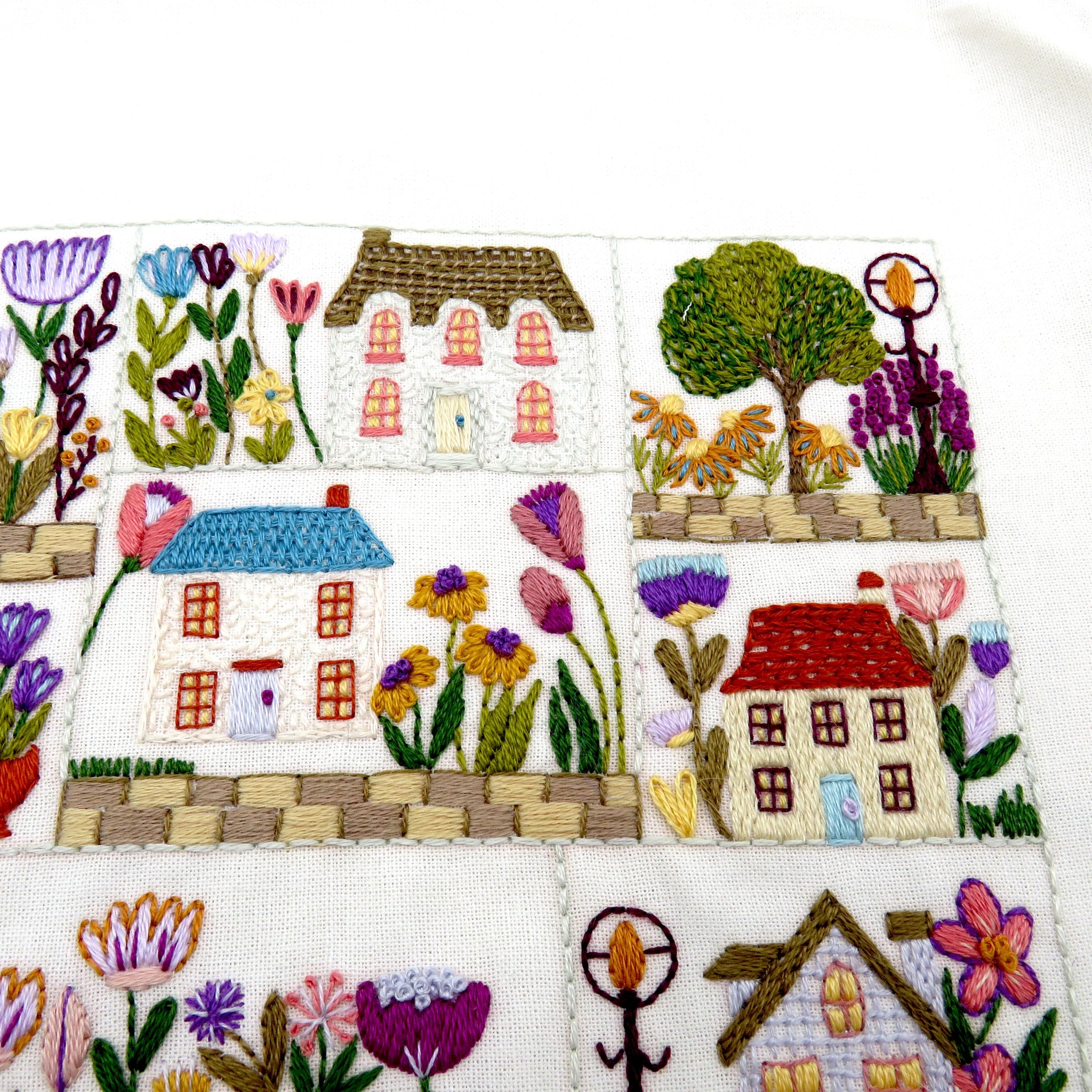 Embroidered panel with houses, trees, and flowers on a white background
