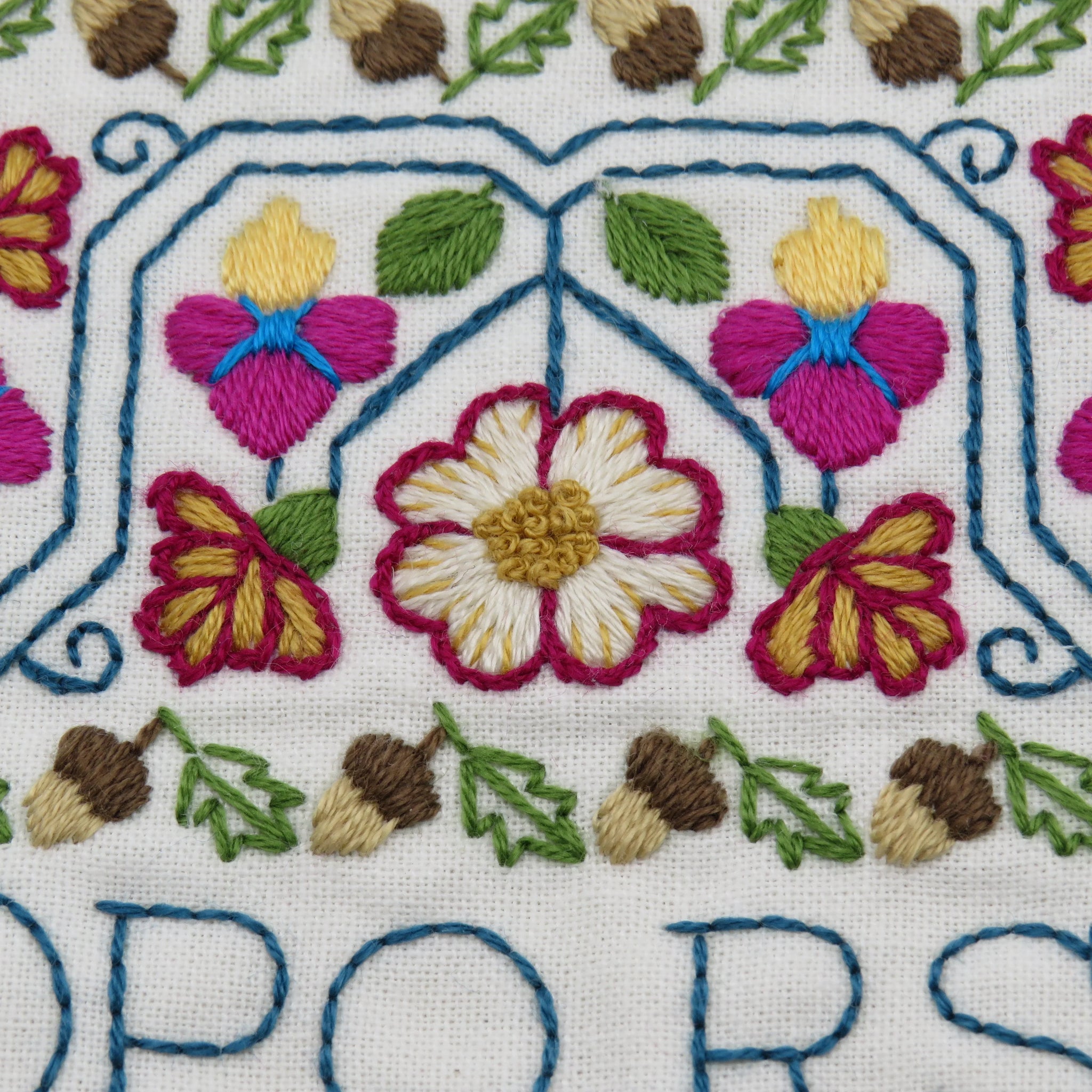 Colorful hand embroidery pattern with flowers, leaves, and acorns on white fabric
