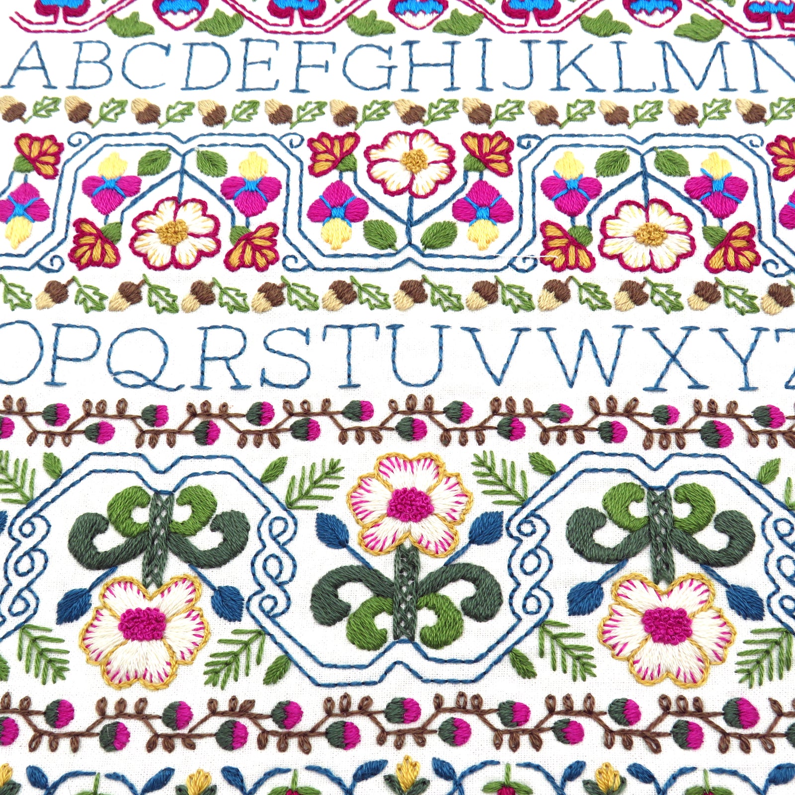 Close-up of a white fabric with colorful embroidered borders and rows of embroidered alphabet letters A through Z.