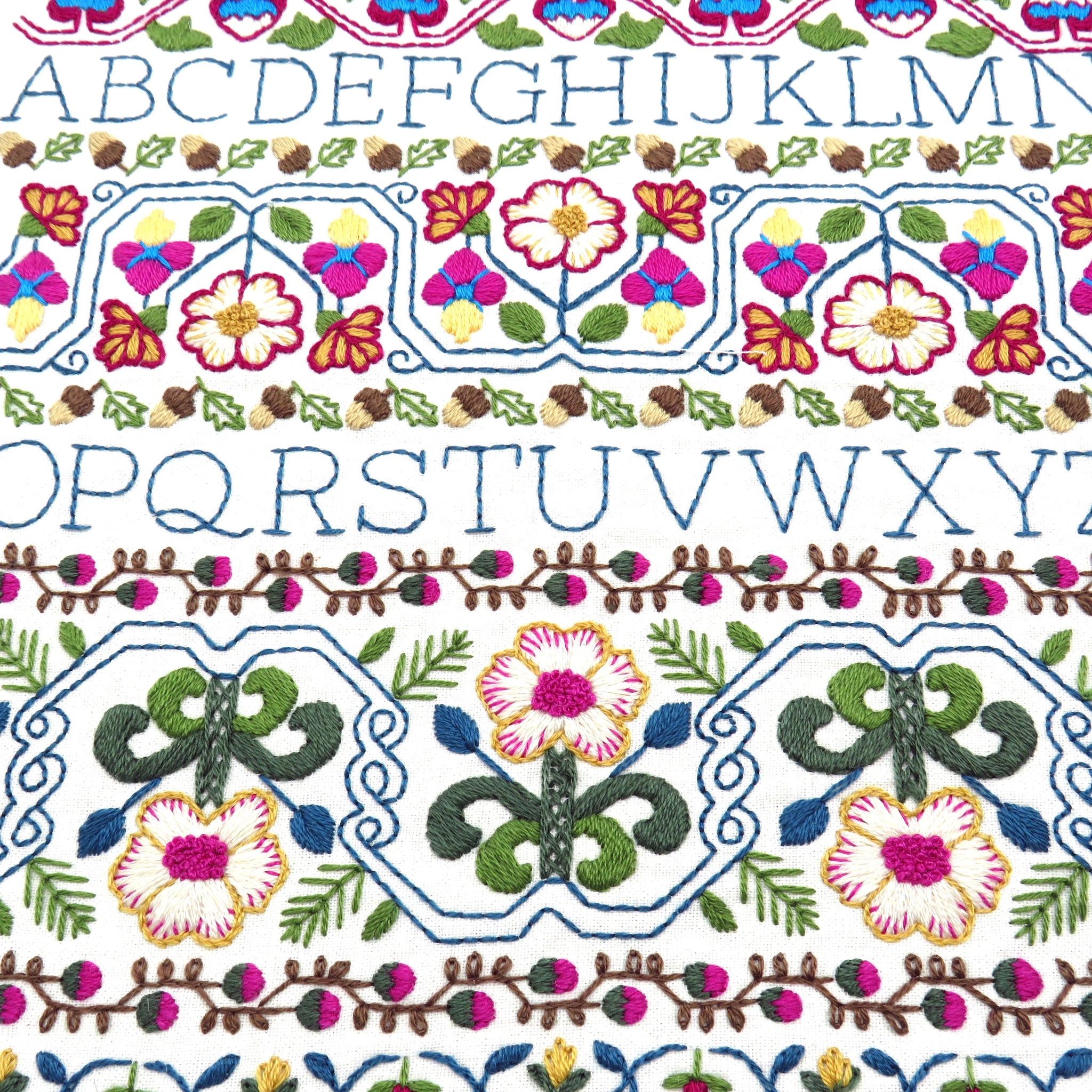 Close-up of a white fabric with colorful embroidered borders and rows of embroidered alphabet letters A through Z.