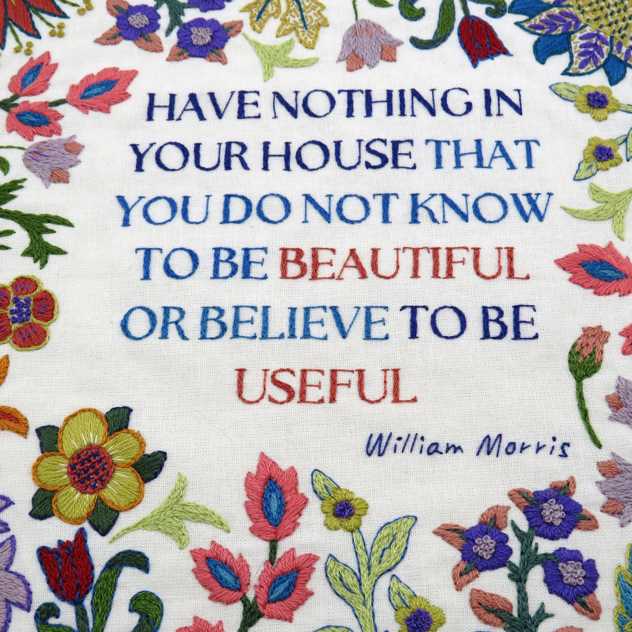 Decorative fabric with embroidered flowers and a quote by William Morris.