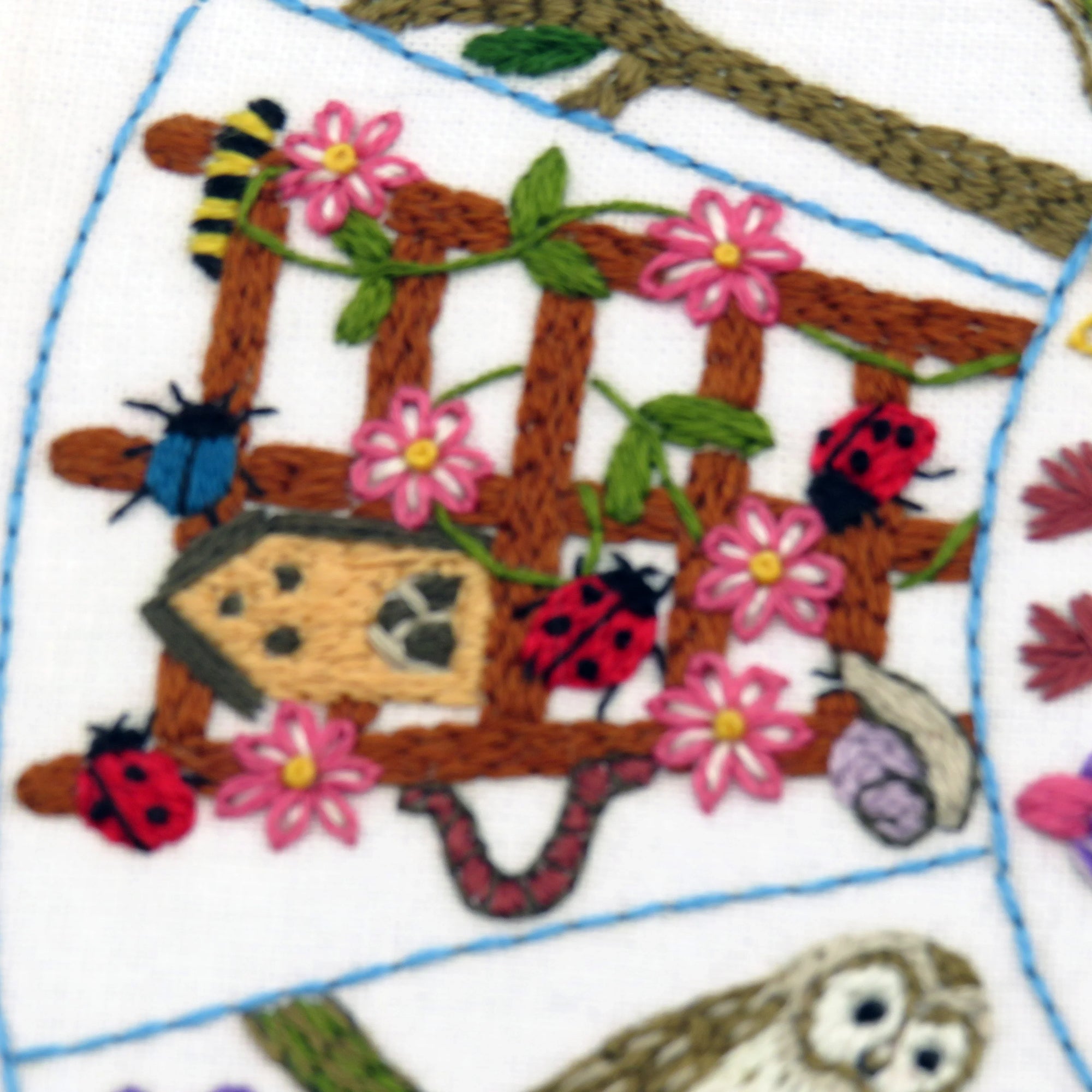 Embroidered design with flowers, ladybugs, and an owl on a white background