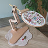 Wooden embroidery hoop stand with a colorful embroidery design on a wooden table.