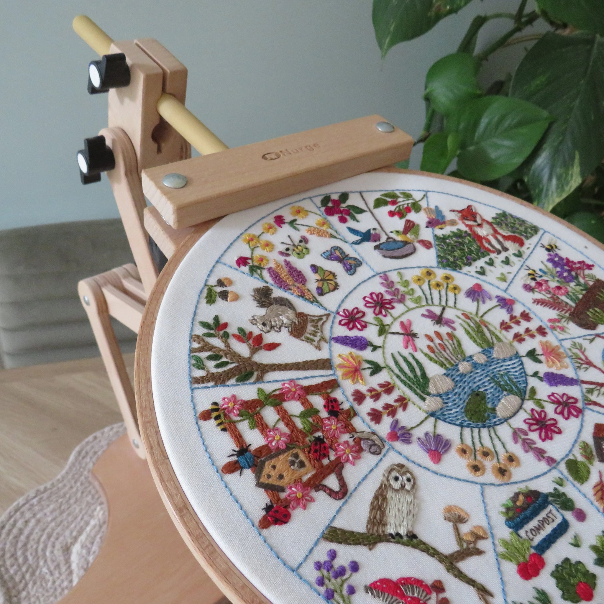 Embroidery hoop with a colorful floral and nature-themed embroidery design, placed on a wooden surface.