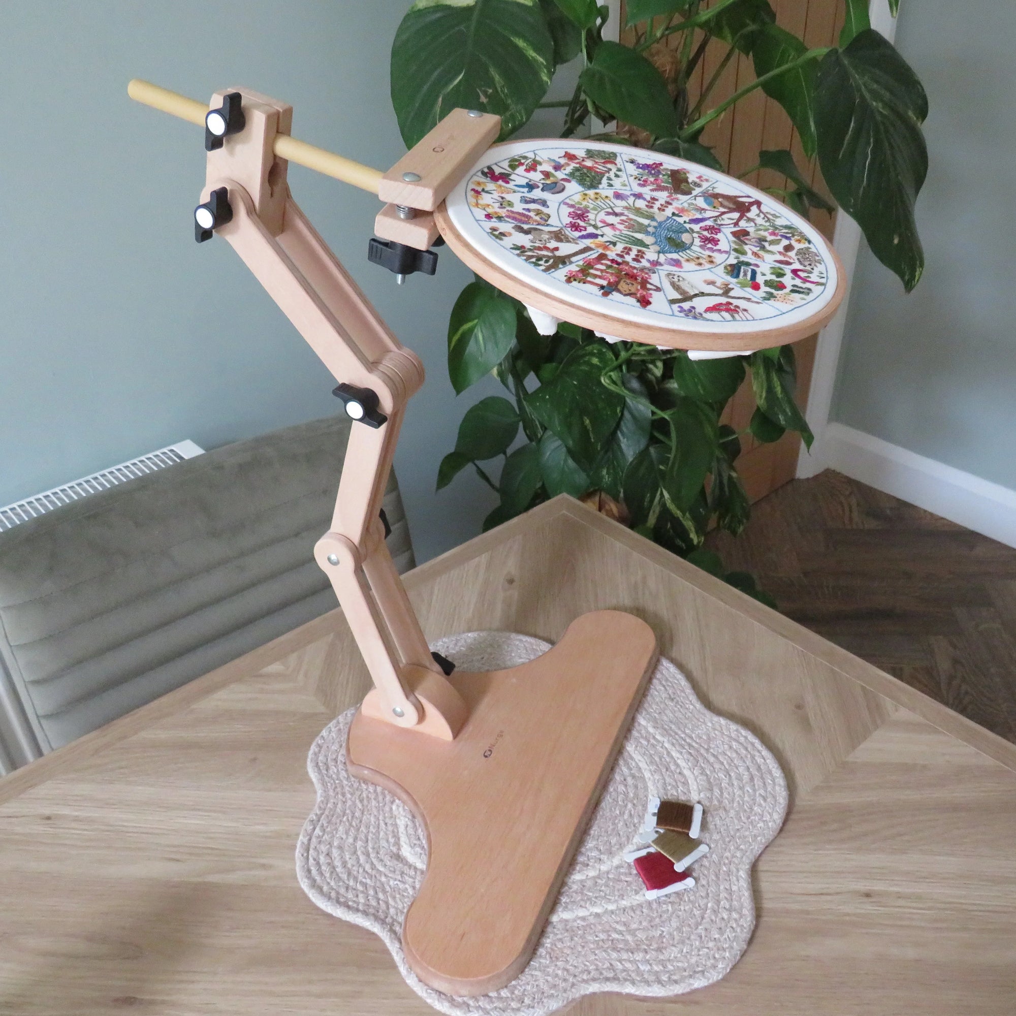 Wooden embroidery hoop stand with a cross-stitched piece on a wooden table.