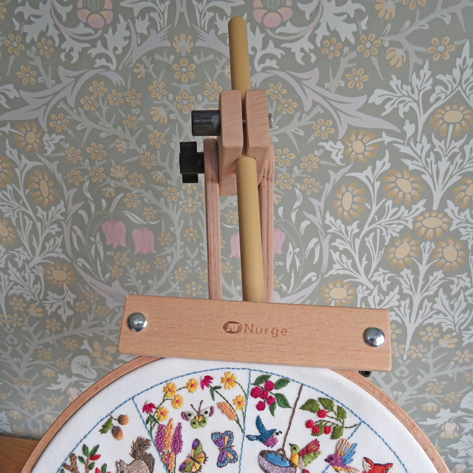 Embroidery hoop with floral design and embroidery tools against a floral-patterned wall.