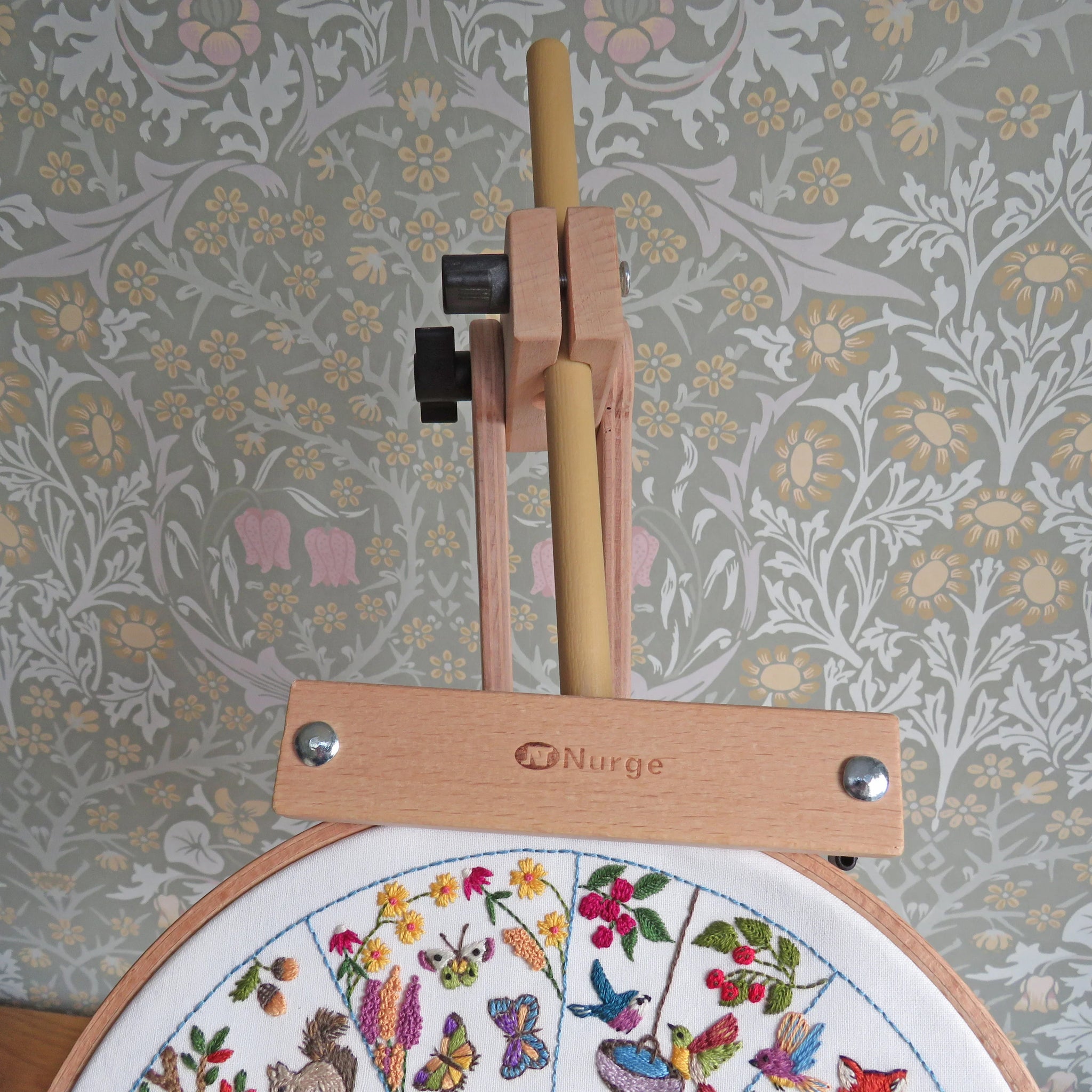 Embroidery hoop with floral design and embroidery tools against a floral-patterned wall.
