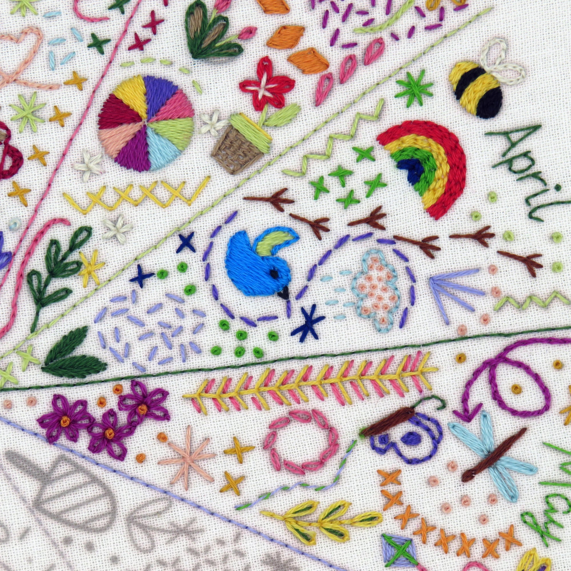 Embroidered fabric with colorful floral and nature-themed designs, including a rainbow and a bee.