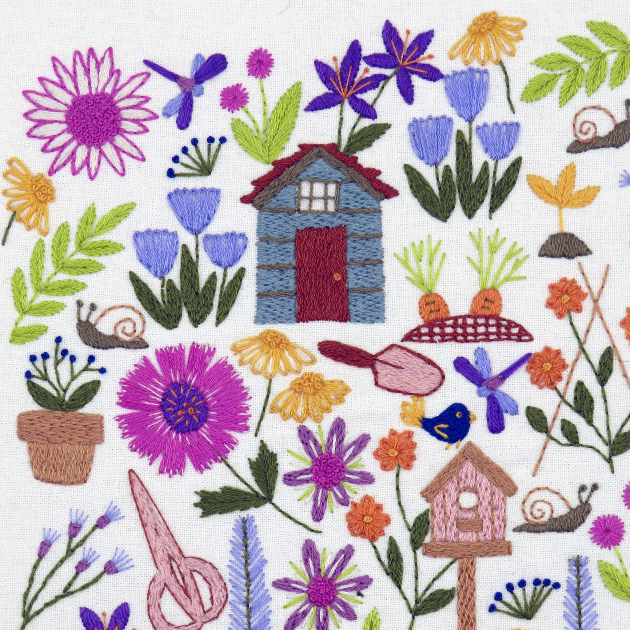 Embroidered design with flowers, a small house, and various elements on a white background