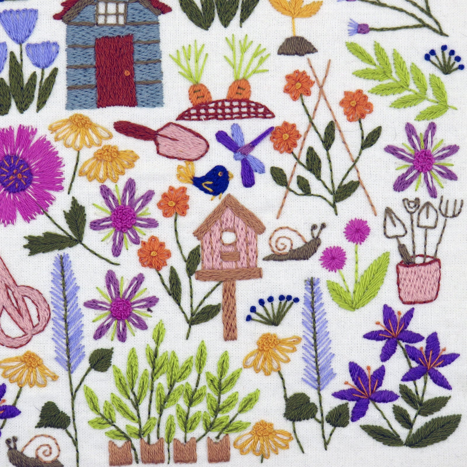 Embroidered fabric with garden-themed design including flowers, plants, a birdhouse, and gardening tools on a white background.