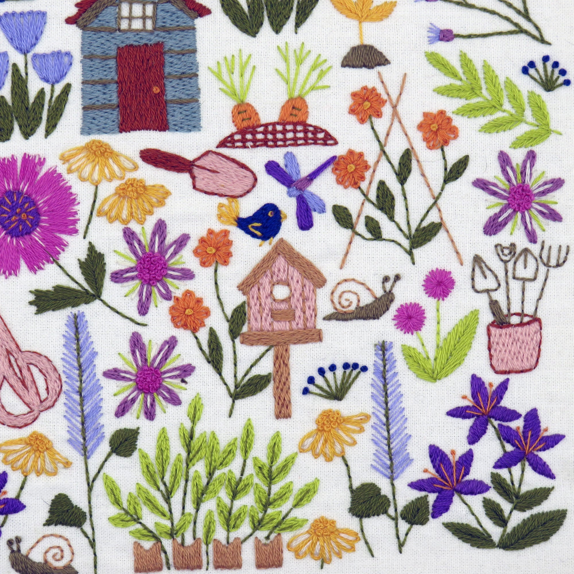 Embroidered fabric with garden-themed design including flowers, plants, a birdhouse, and gardening tools on a white background.