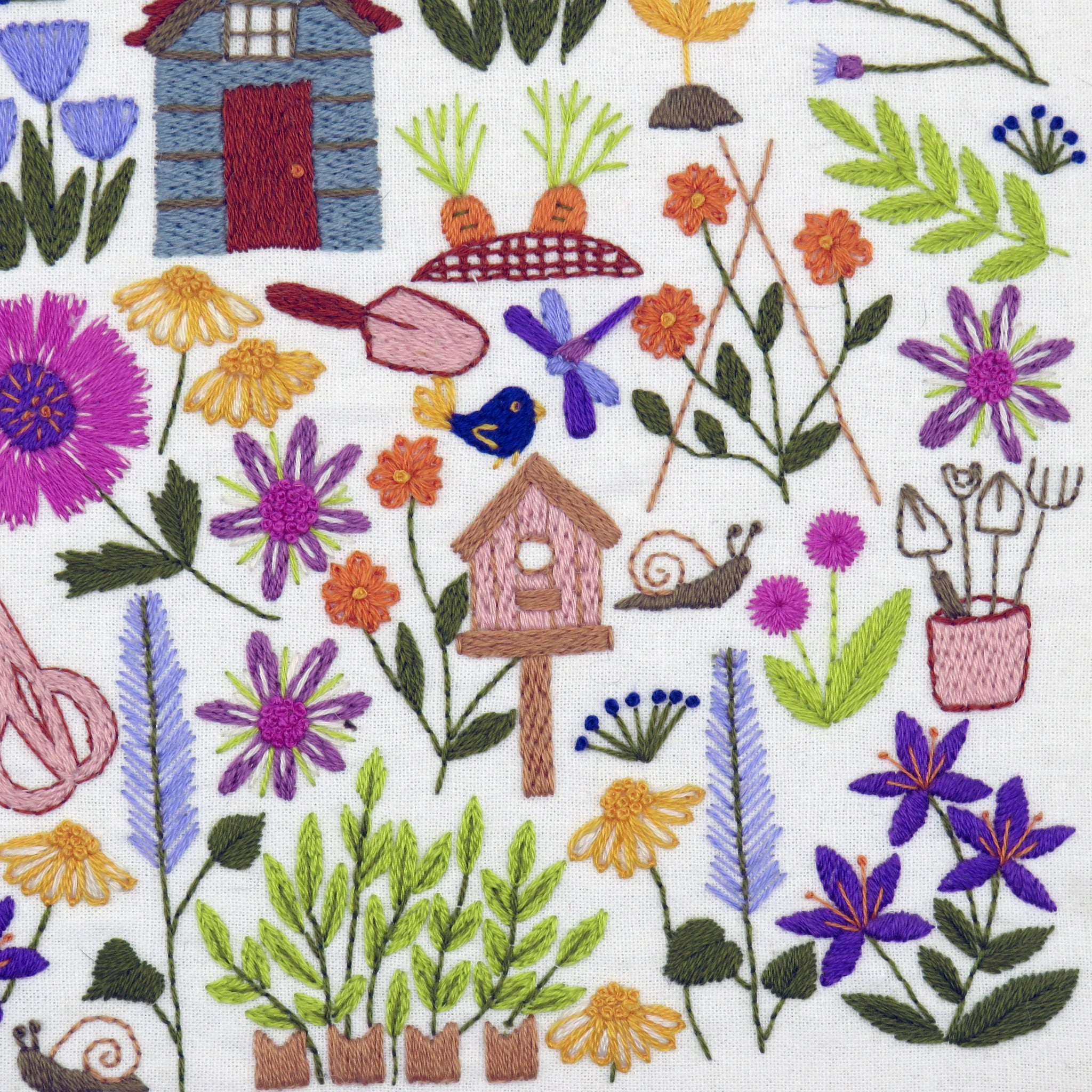 Embroidered fabric with garden-themed design including flowers, plants, a birdhouse, and gardening tools on a white background.