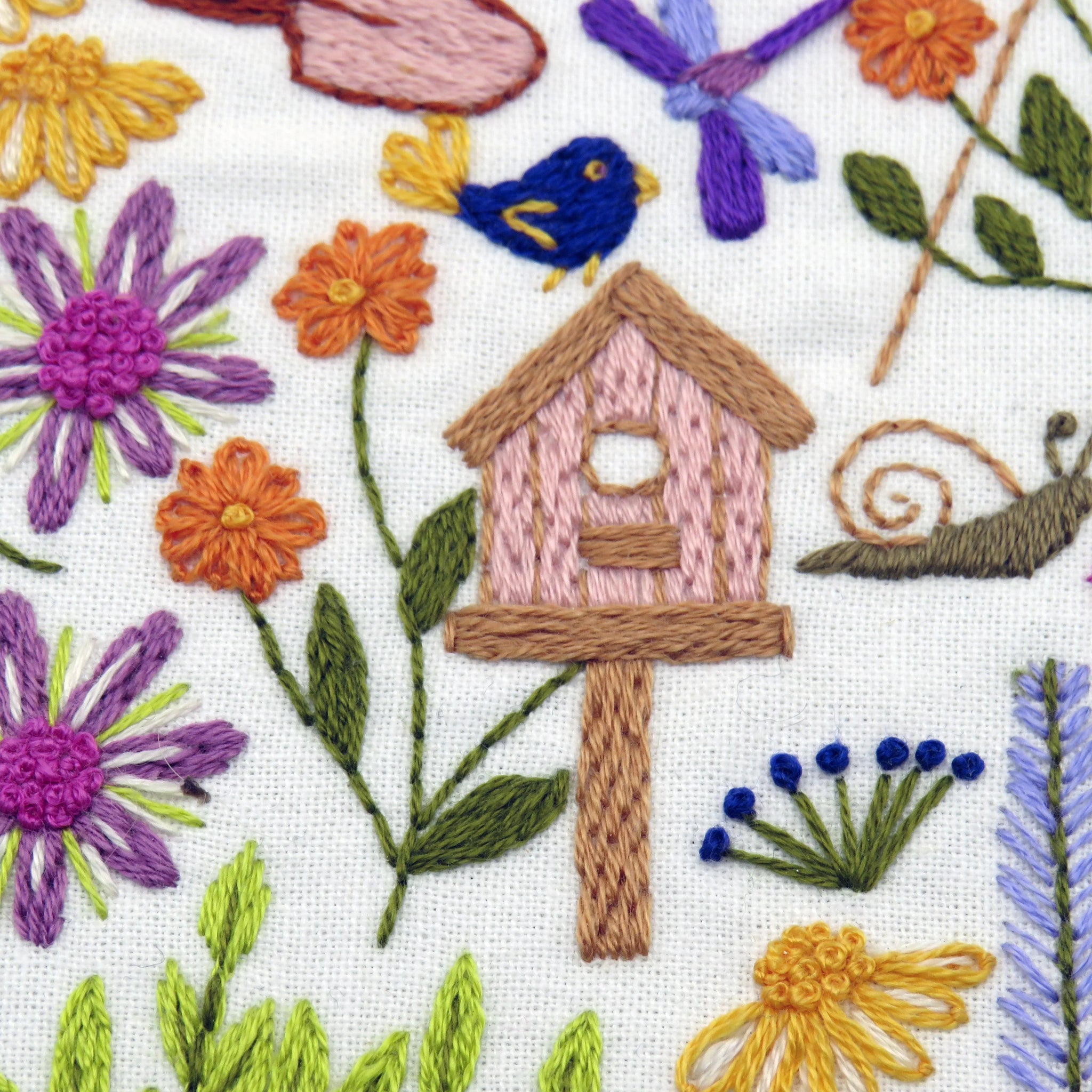 Embroidered design of a birdhouse with flowers and a bird.