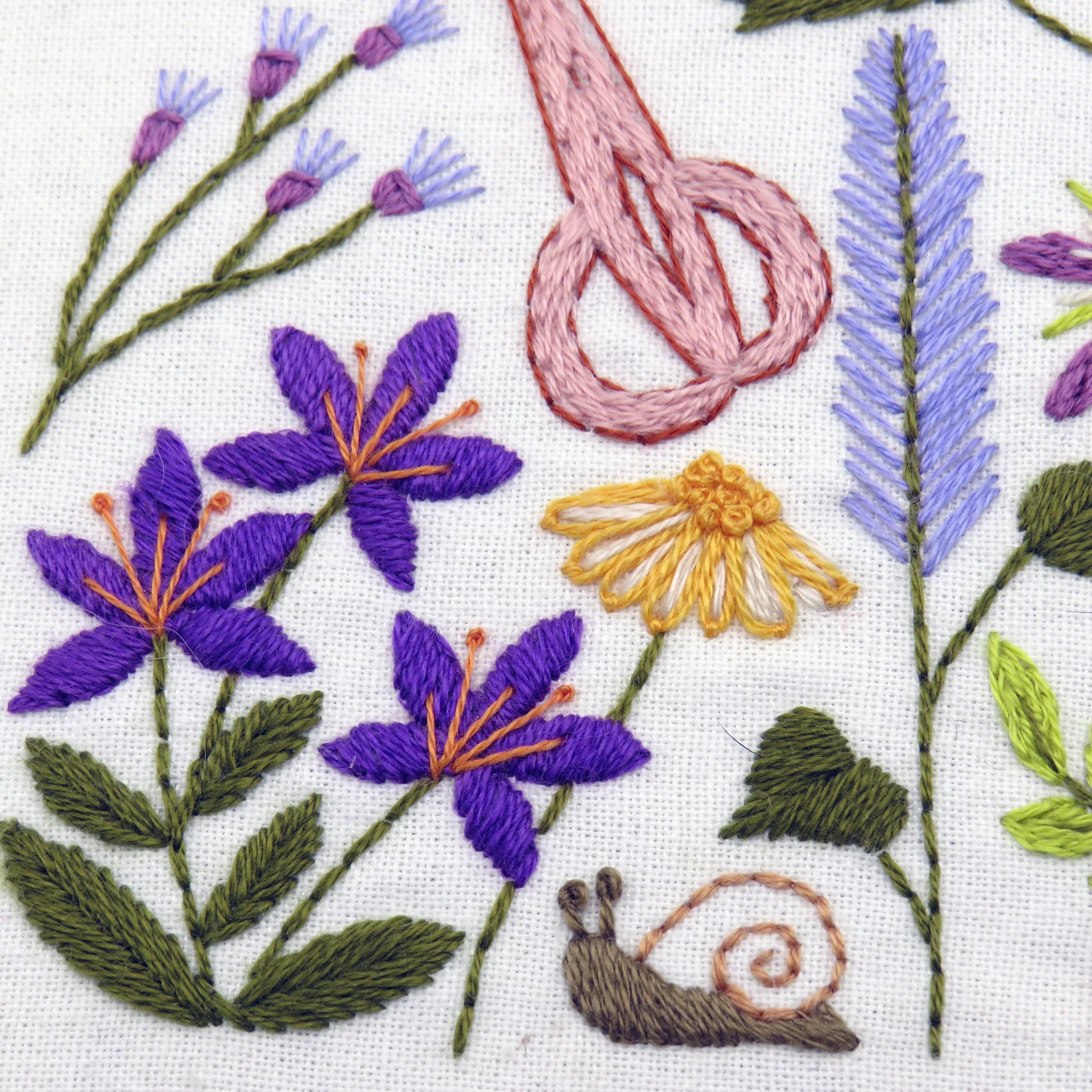 Embroidered design with flowers, leaves, and a snail on white fabric.