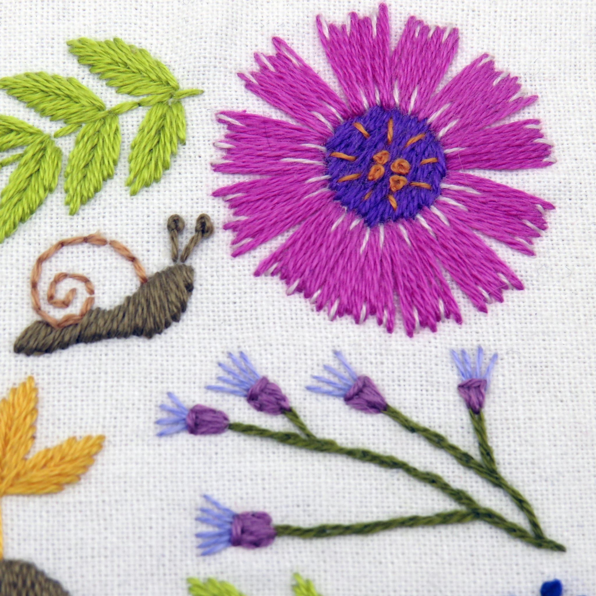 Embroidered design of a purple flower, green leaves, and a snail on a white background.