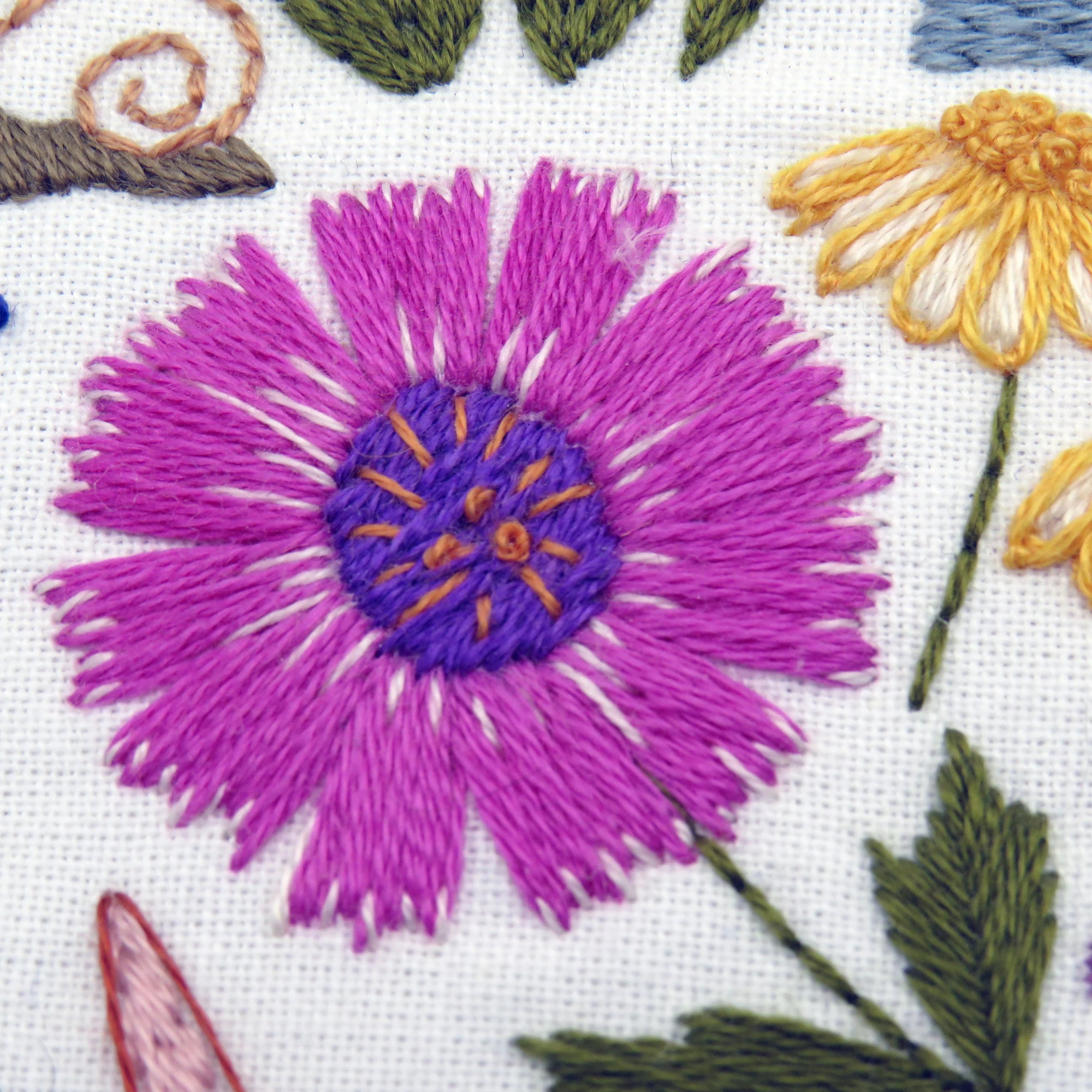 Embroidered flowers including a purple flower with a yellow center on a white background.