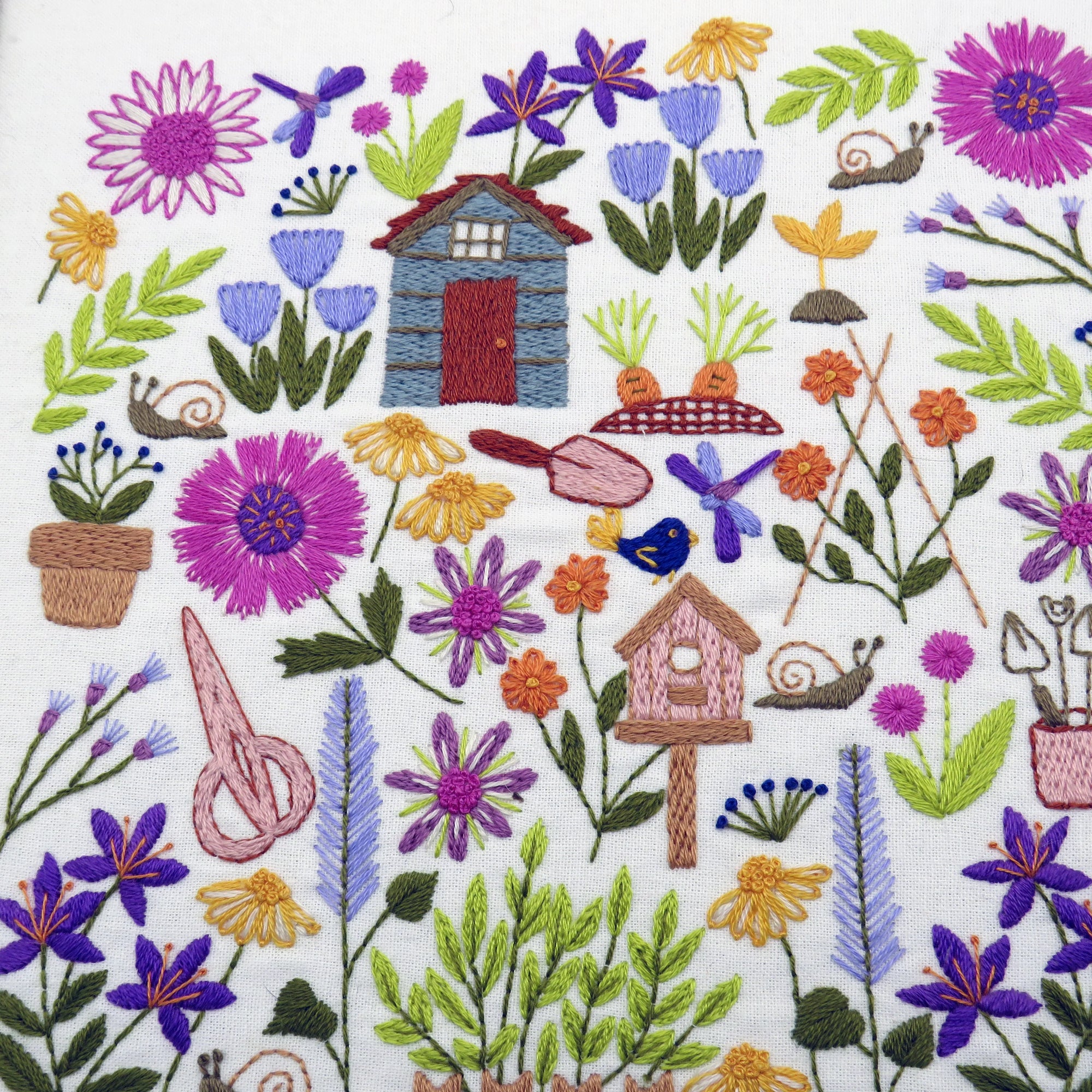 Embroidered design with flowers, plants, and small structures on a white background