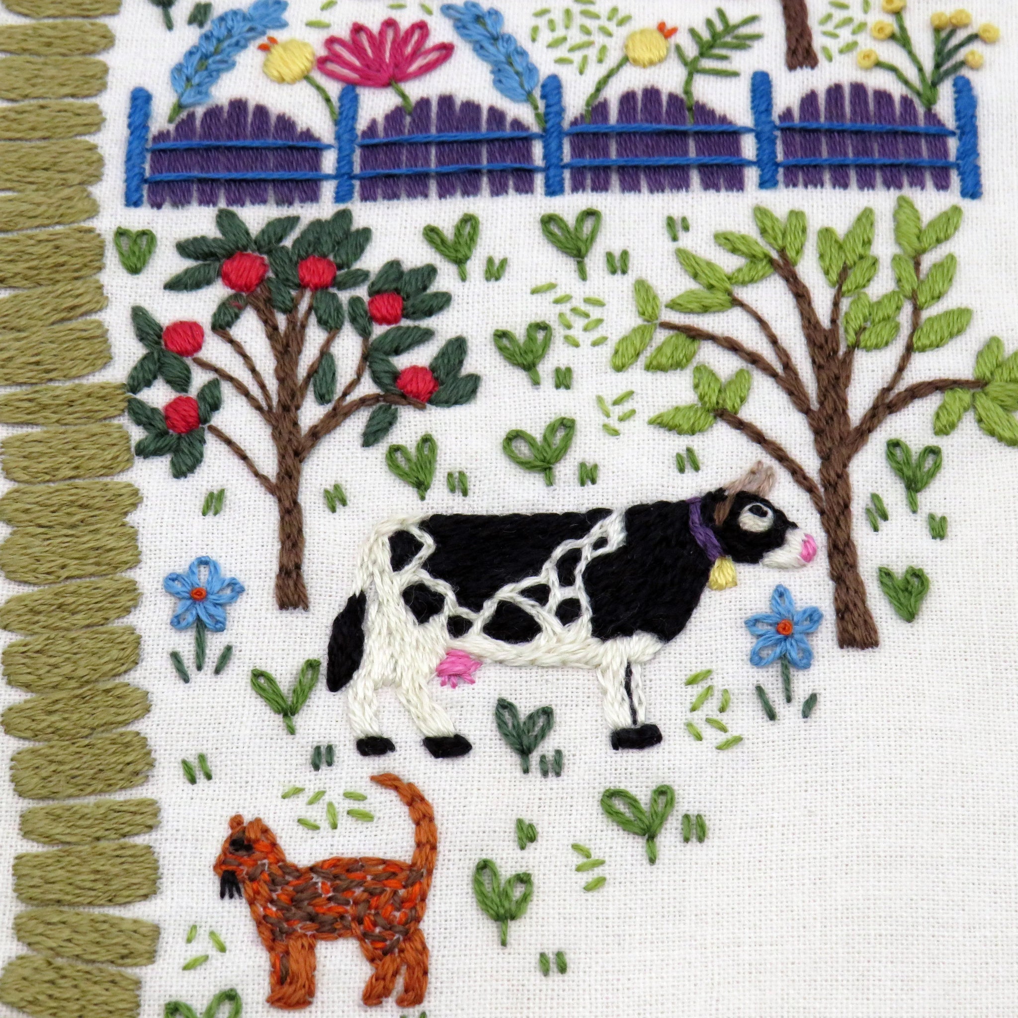 Embroidered design of a cow and cat in a garden with flowers and trees.