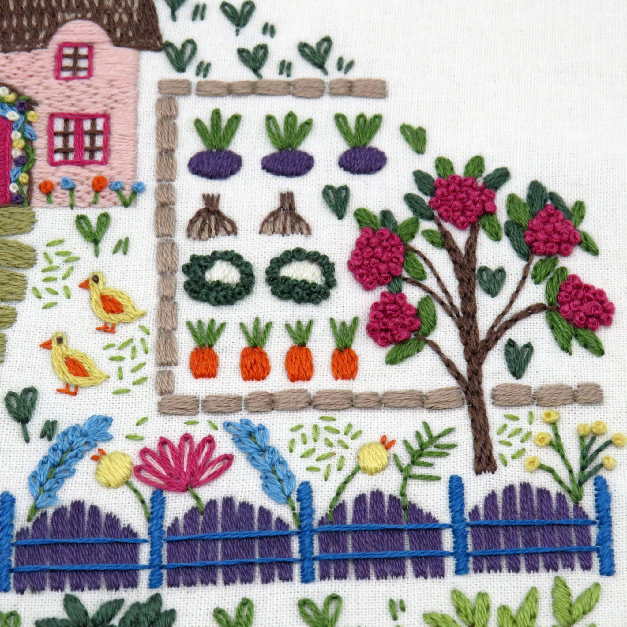 Embroidered scene with a house, garden, and animals on a white background