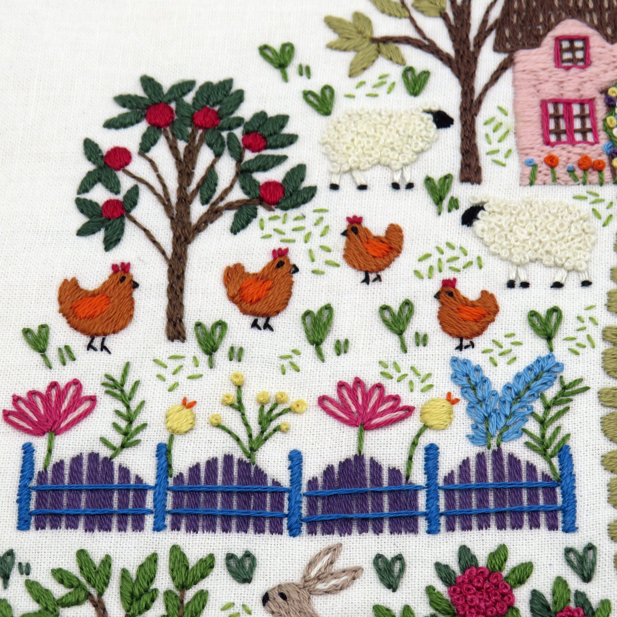 Embroidered design of a pastoral scene with sheep, chickens, flowers, and a house.