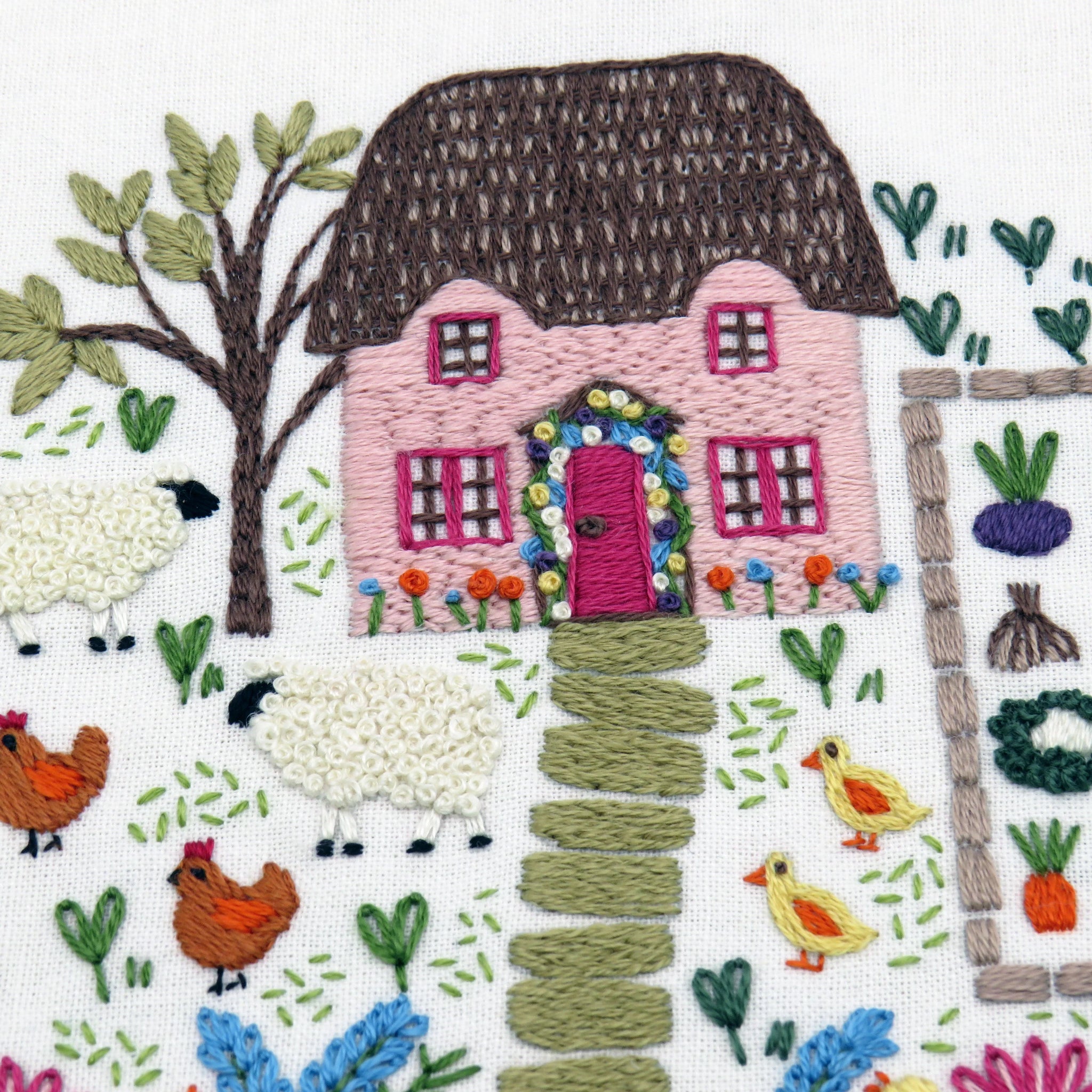 Embroidered design of a pink house with a thatched roof, sheep, chickens, and ducks in a garden setting.