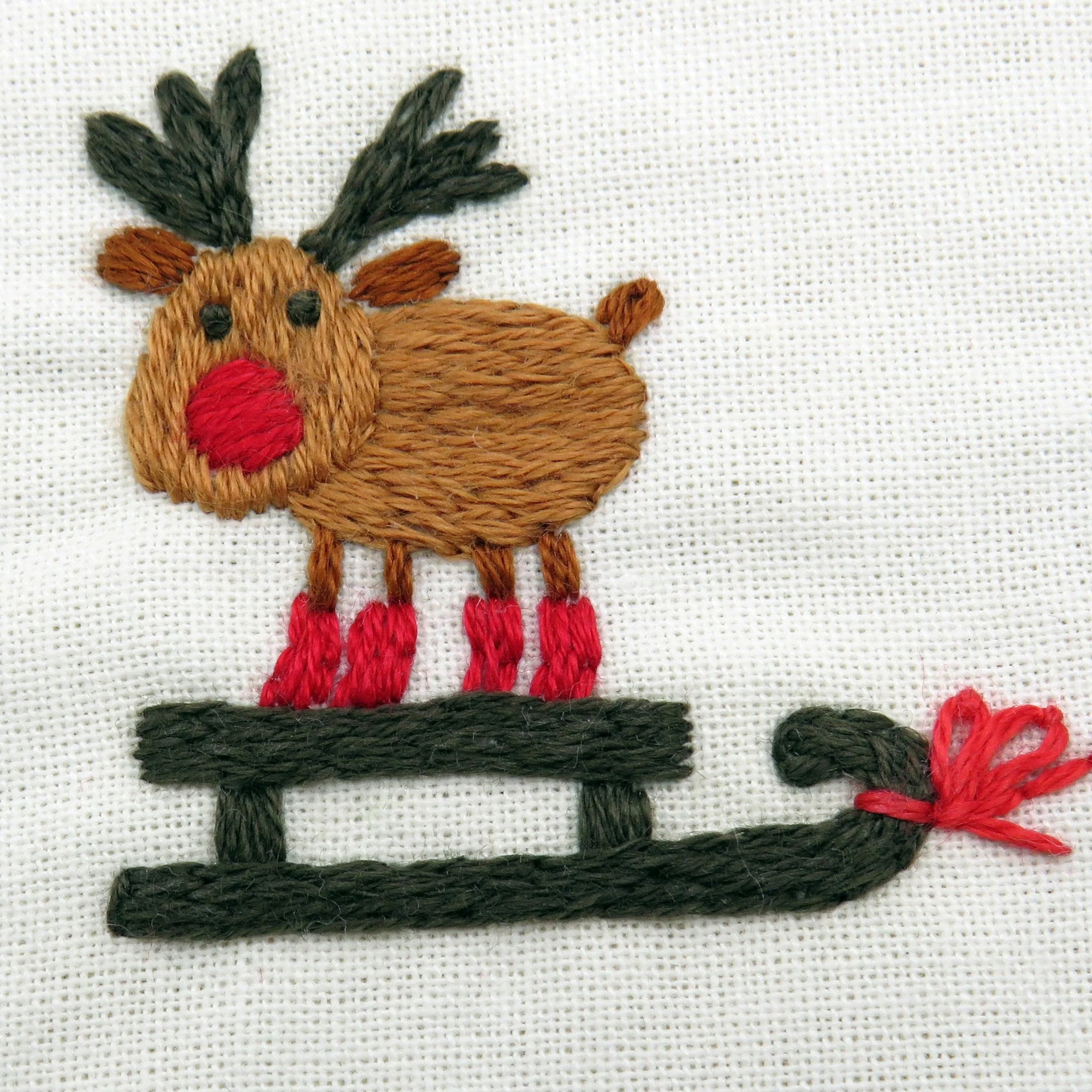 Embroidered reindeer on a white fabric with a red border featuring star patterns.