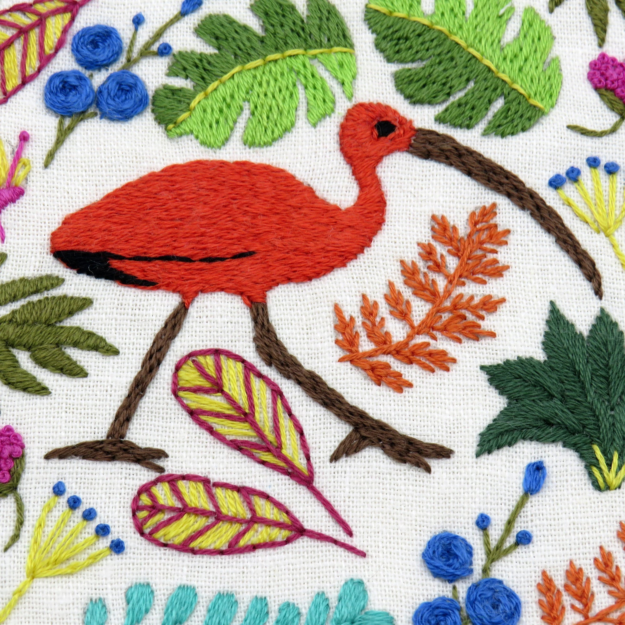 Embroidered design of a red bird surrounded by green leaves and flowers on a white background