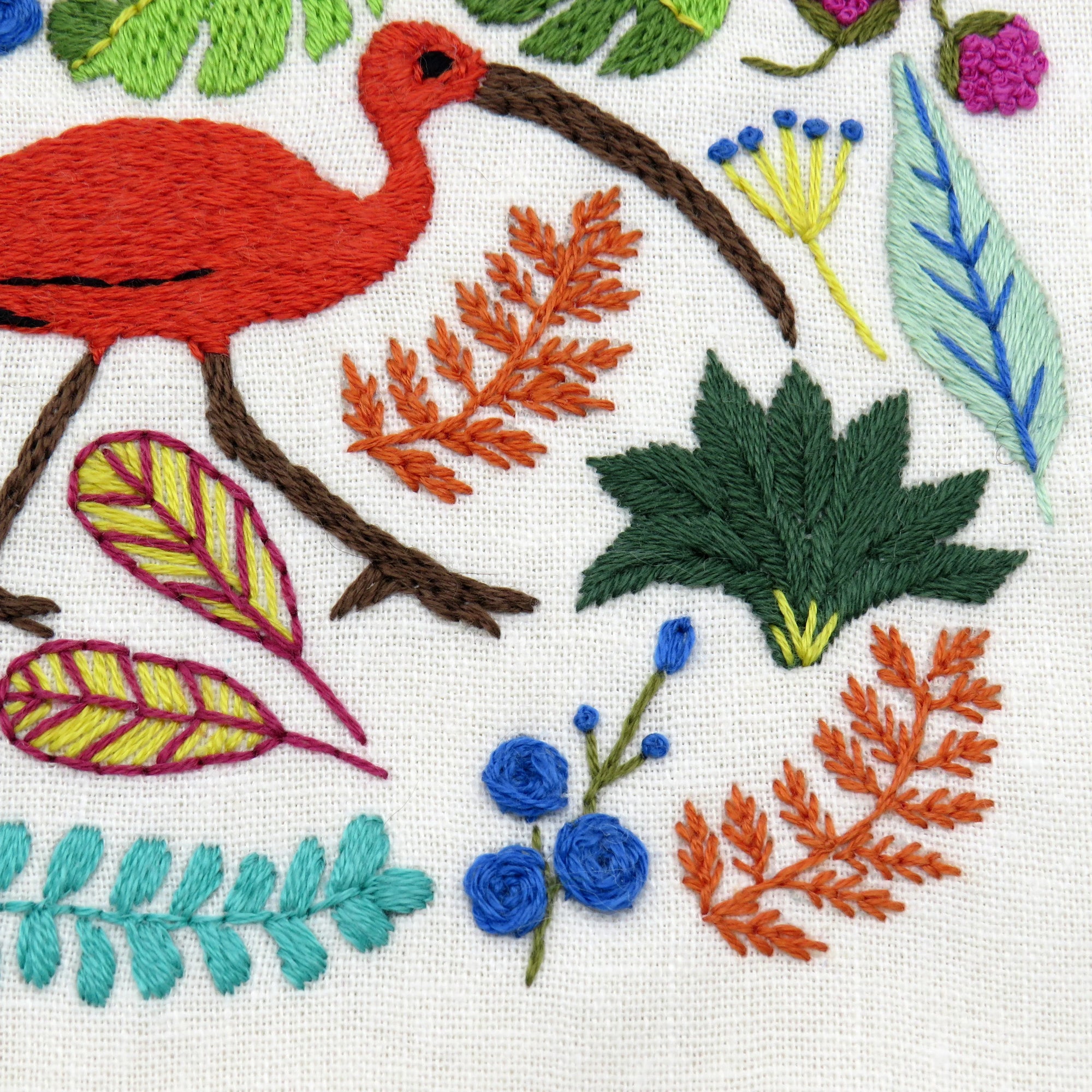Embroidered design of a red bird, leaves, and flowers on a white background