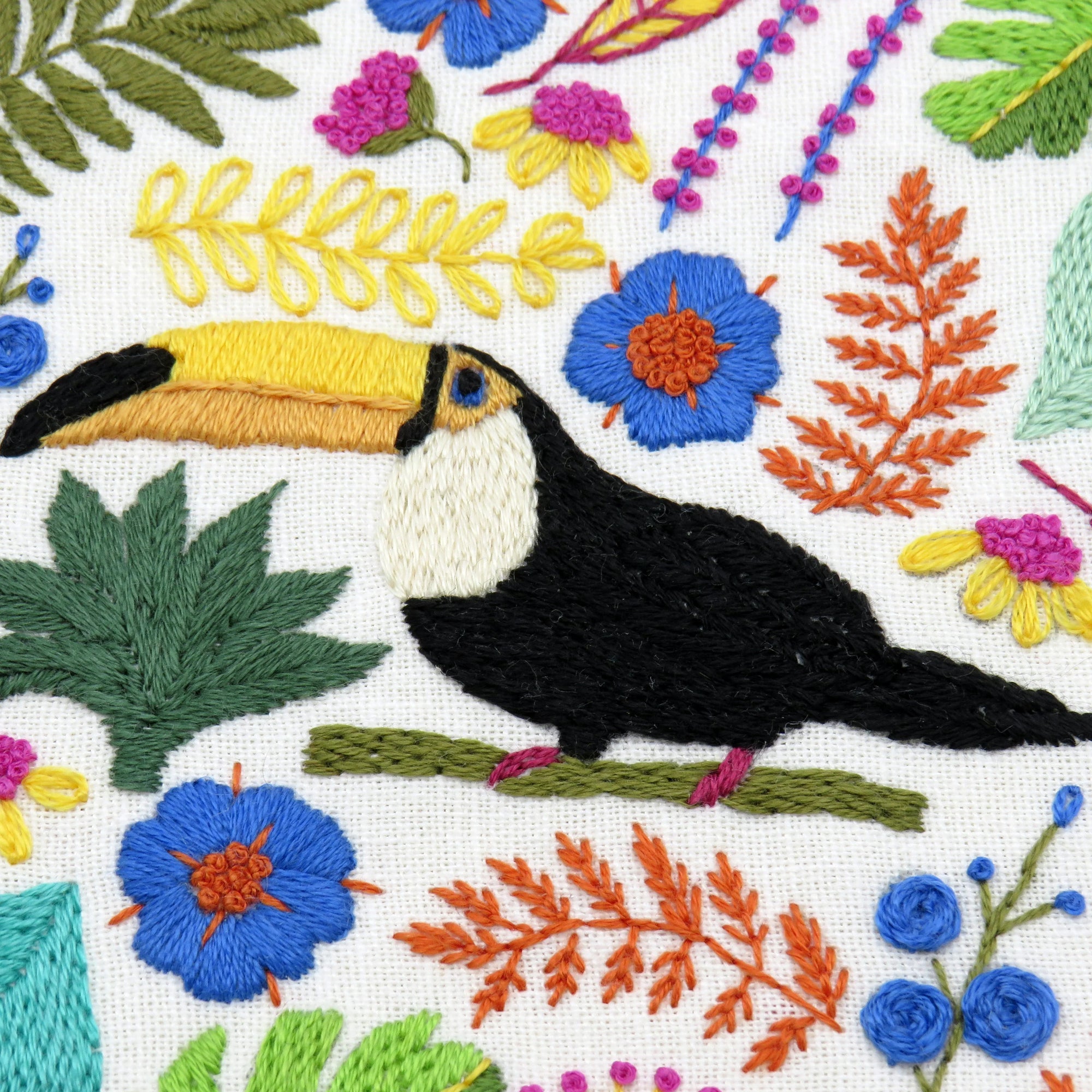 Embroidered design of a toucan surrounded by flowers and leaves on a white background
