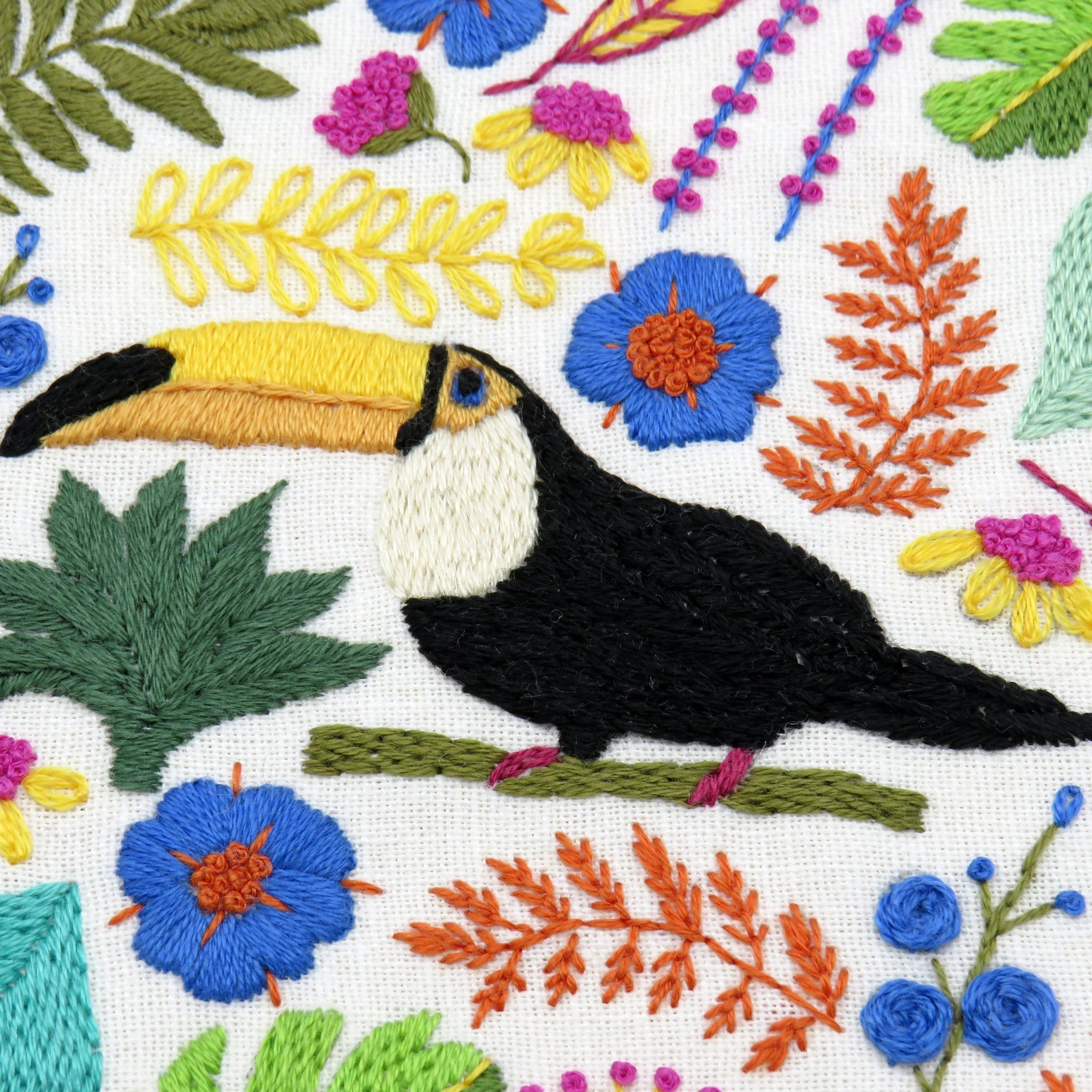 Embroidered design of a toucan surrounded by flowers and leaves on a white background