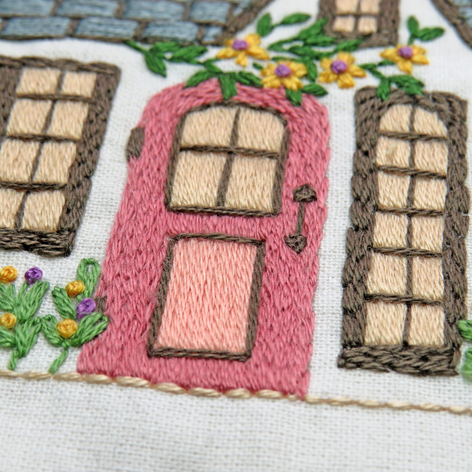 Embroidered design of a pink door with windows and flowers on a white background